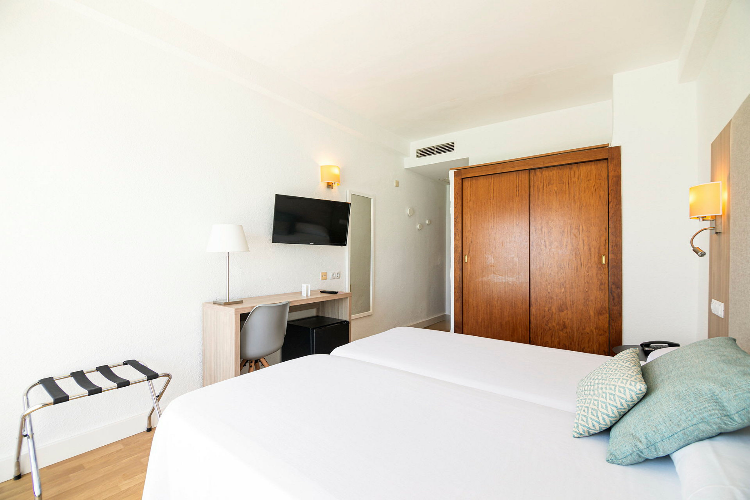Hotelværelse med to enkeltsenge, skrivebord, stol, TV og garderobe. (AI-genereret tekst)