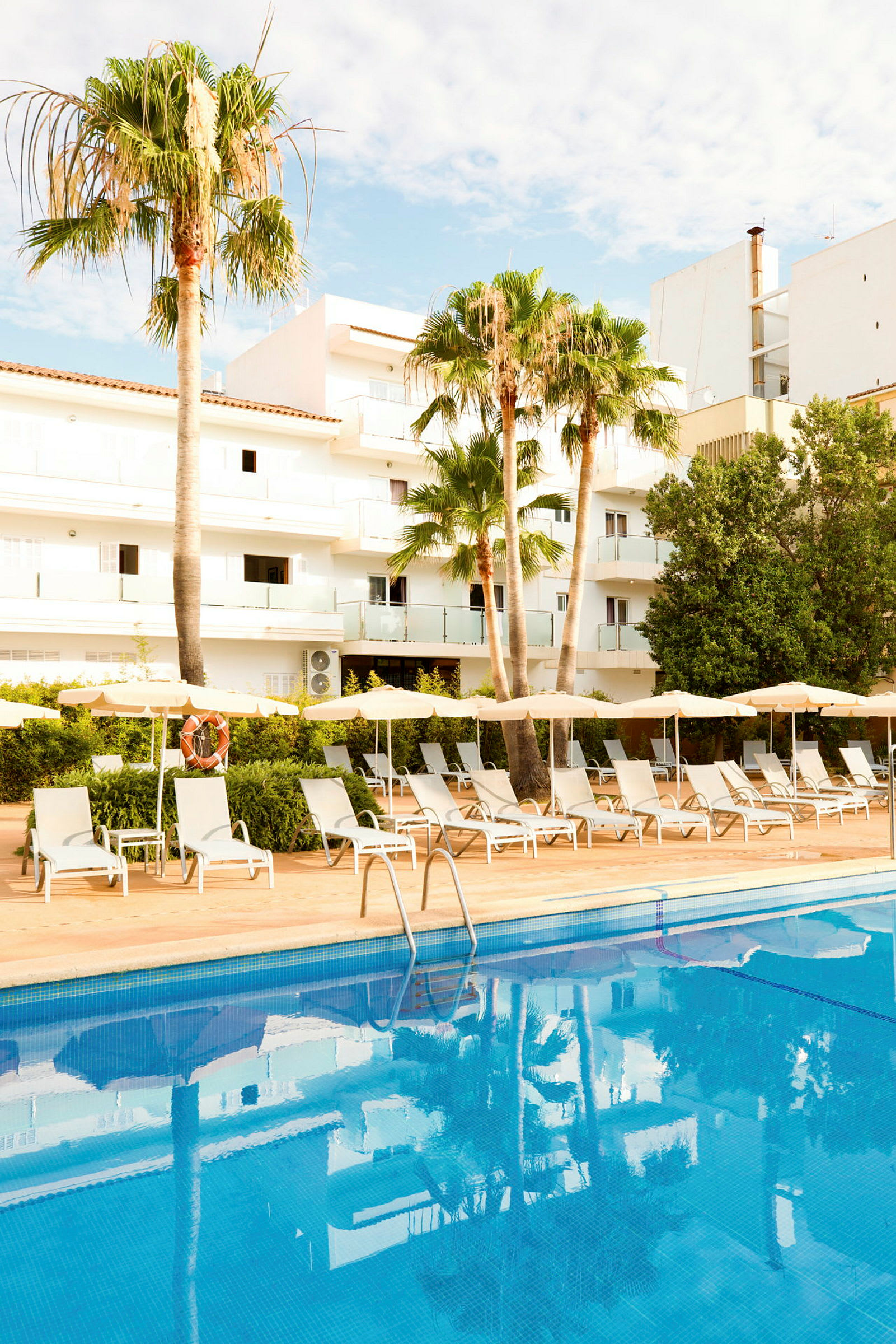 Udendørs swimmingpool med liggestole og parasoller ved et hotelområde med palmer. (AI-genereret tekst)