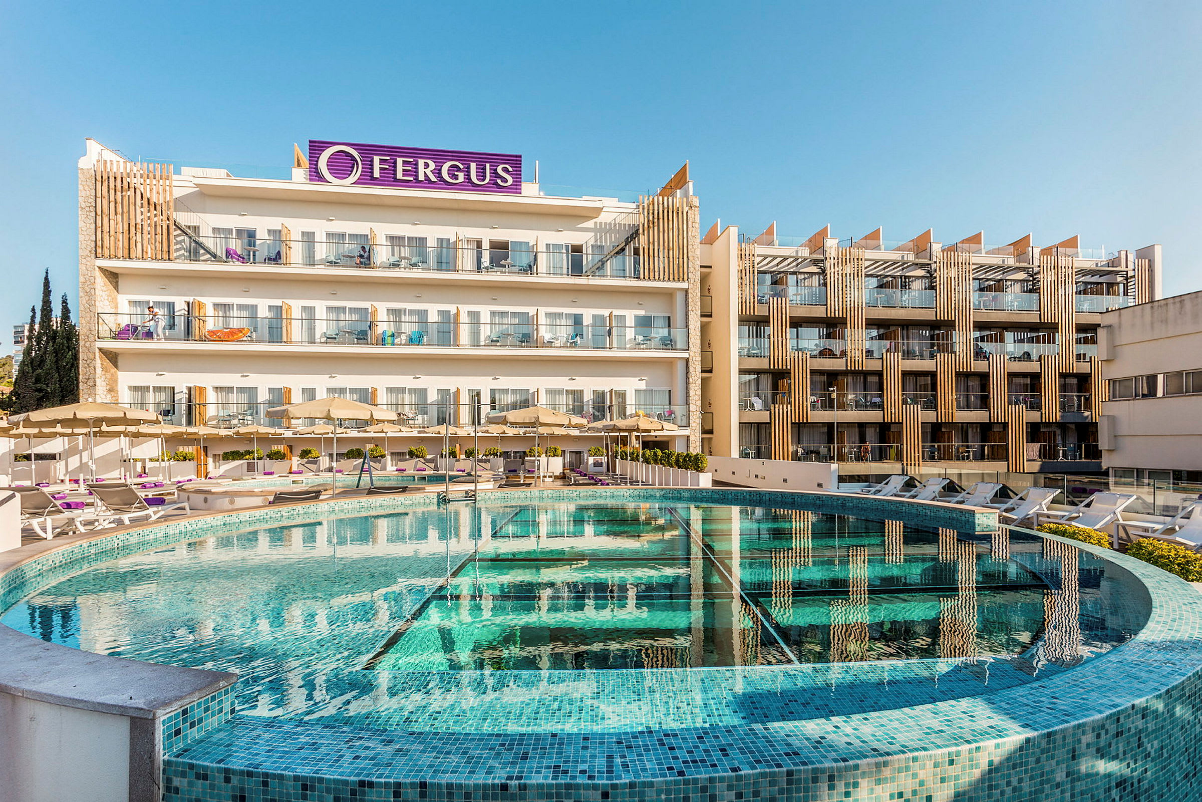 Hotelbygningen med pool og liggestole i forgrunden. (AI-genereret tekst)