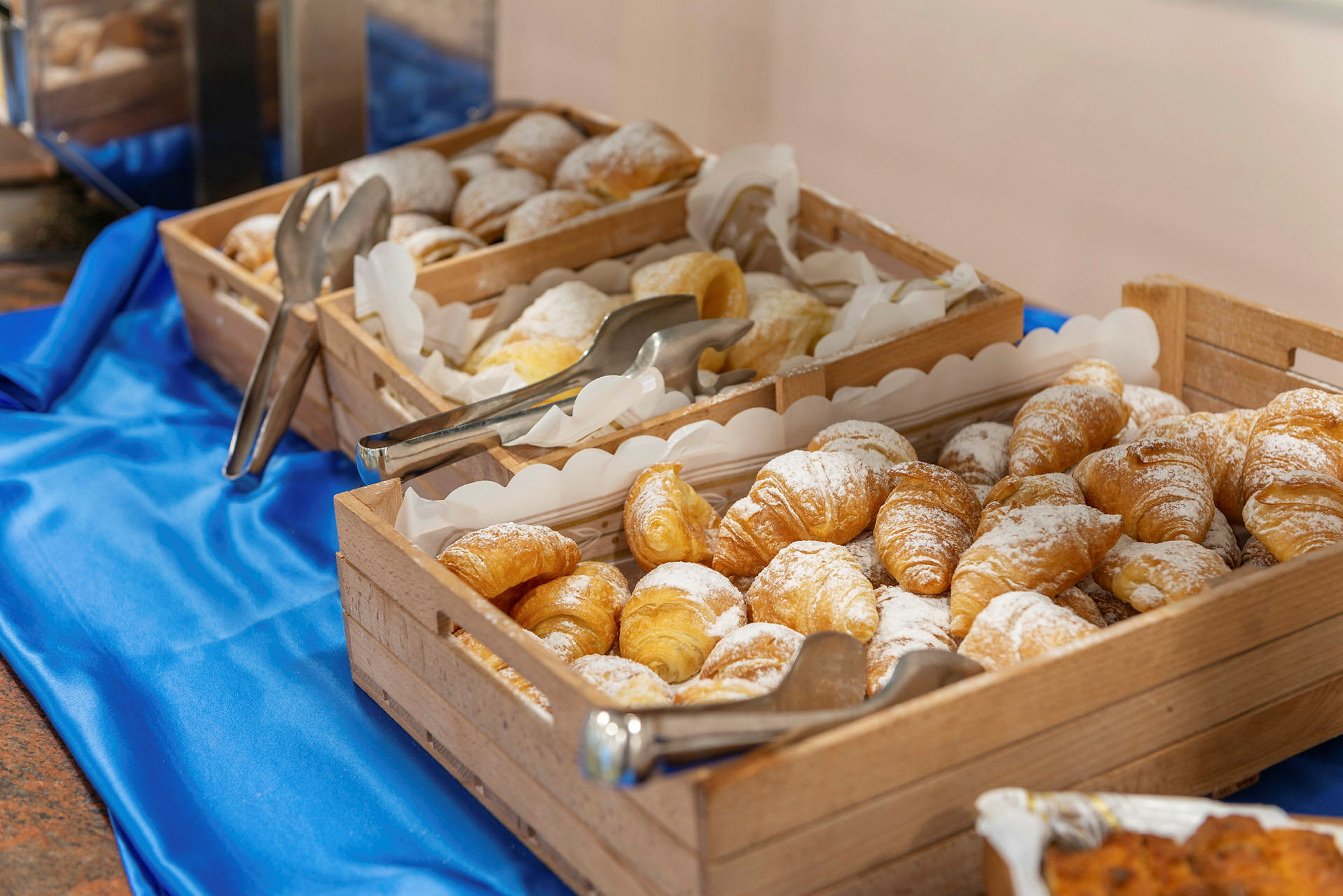 Trækurve fyldt med croissanter, drysset med flormelis, på en blå dug. (AI-genereret tekst)