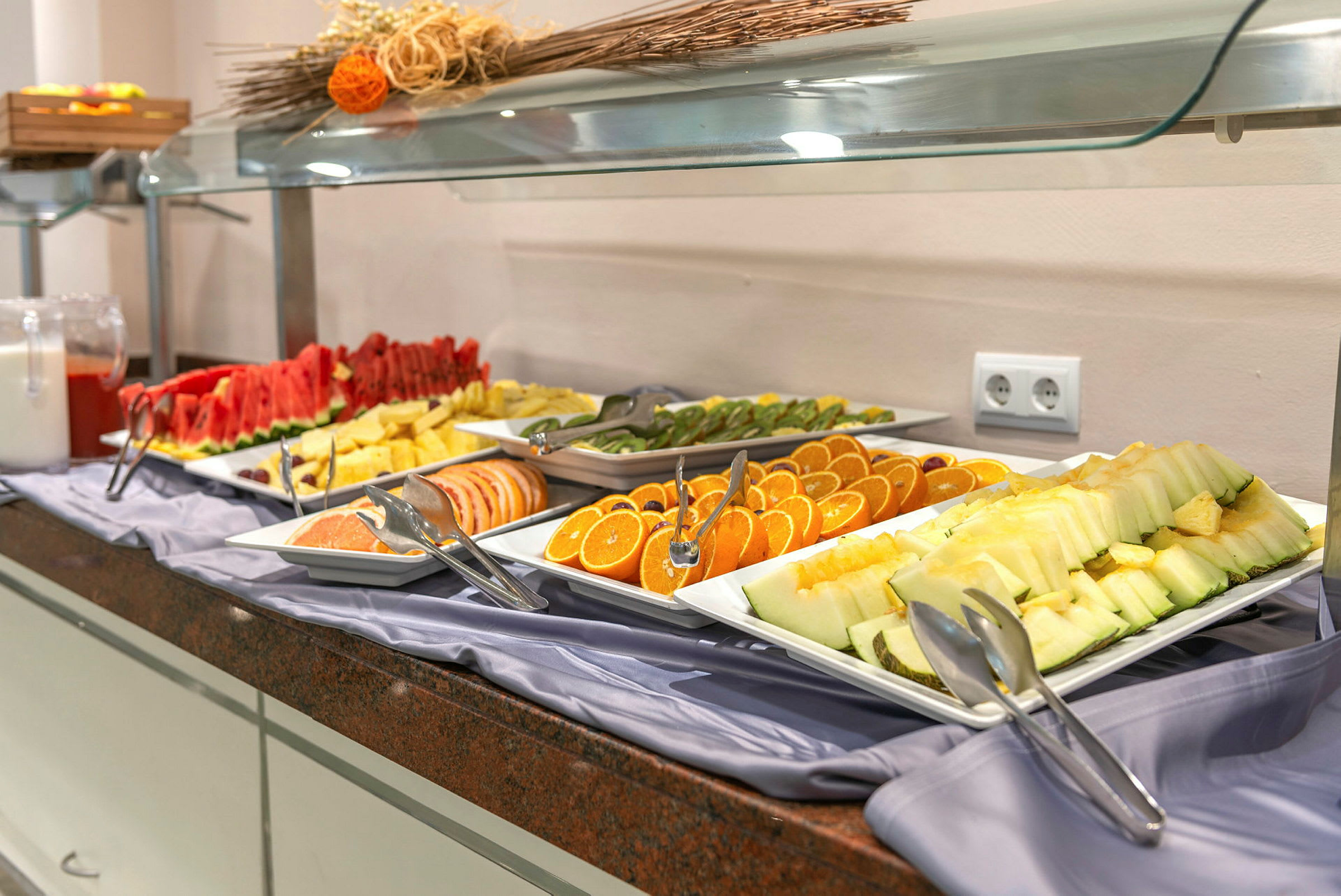 Buffet med frisk skåret frugt, herunder melon, appelsin og kiwi. (AI-genereret tekst)