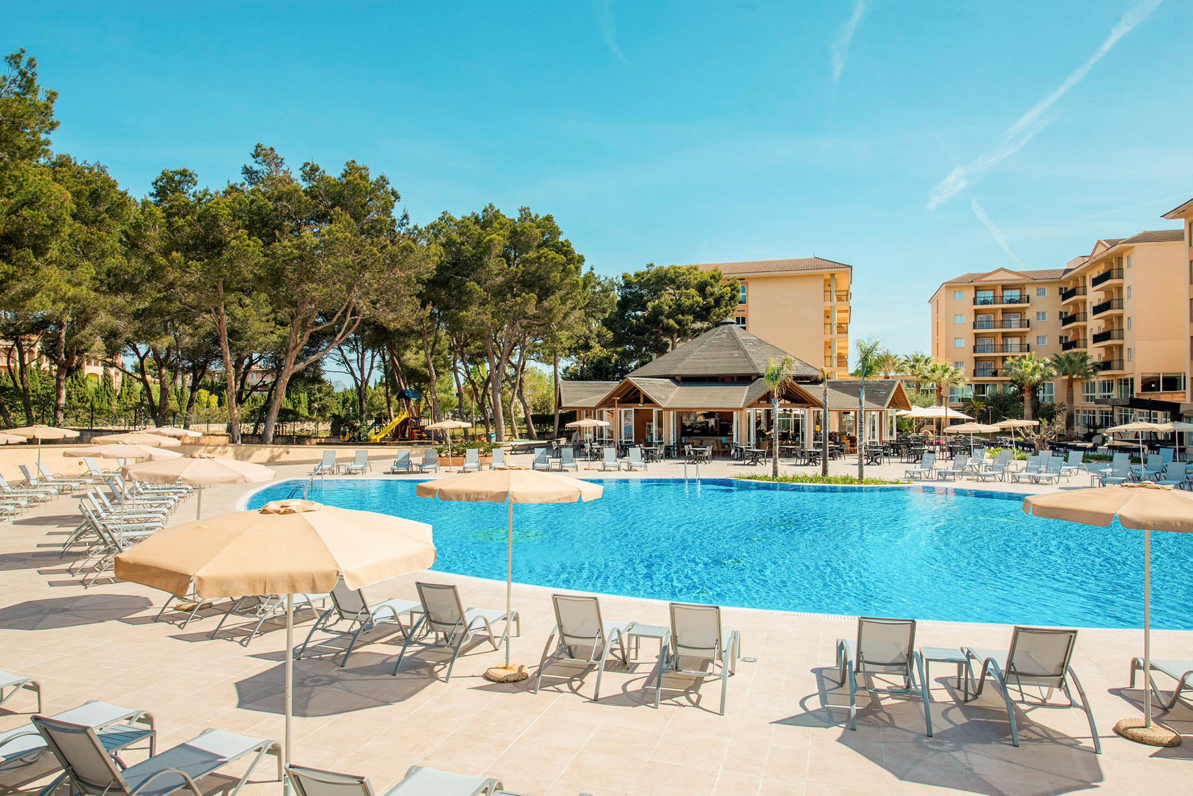 Udendørs pool omgivet af liggestole og parasoller, med hotellet i baggrunden. (AI-genereret tekst)
