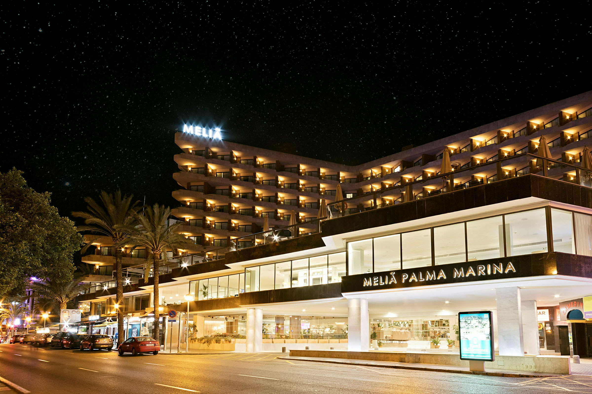 Et hotel ved en gade om aftenen, med lys fra bygningen og stjerneklar himmel. (AI-genereret tekst)