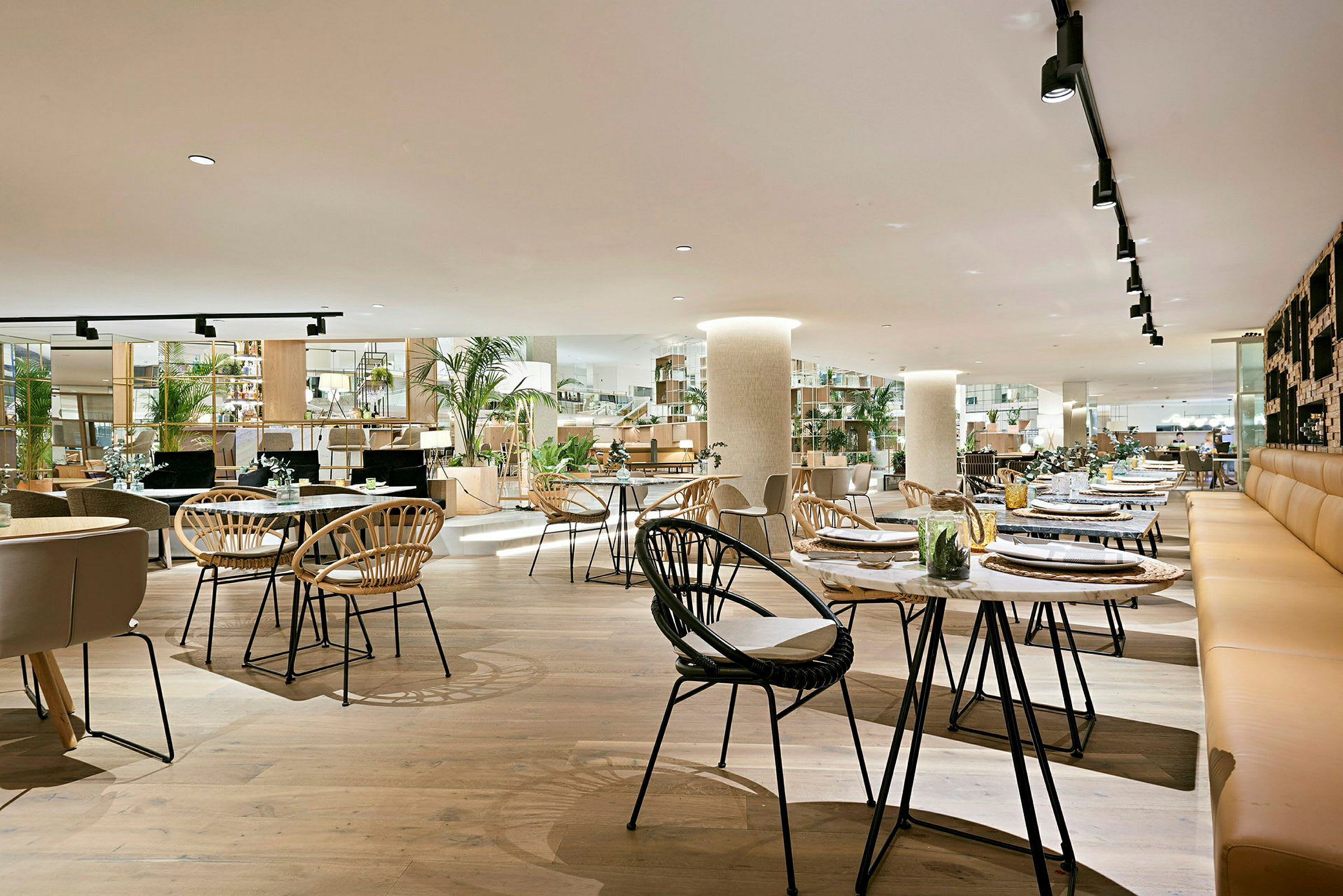 En rummelig restaurant med moderne interiør, træborde og stole samt grønne planter som dekoration. (AI-genereret tekst)