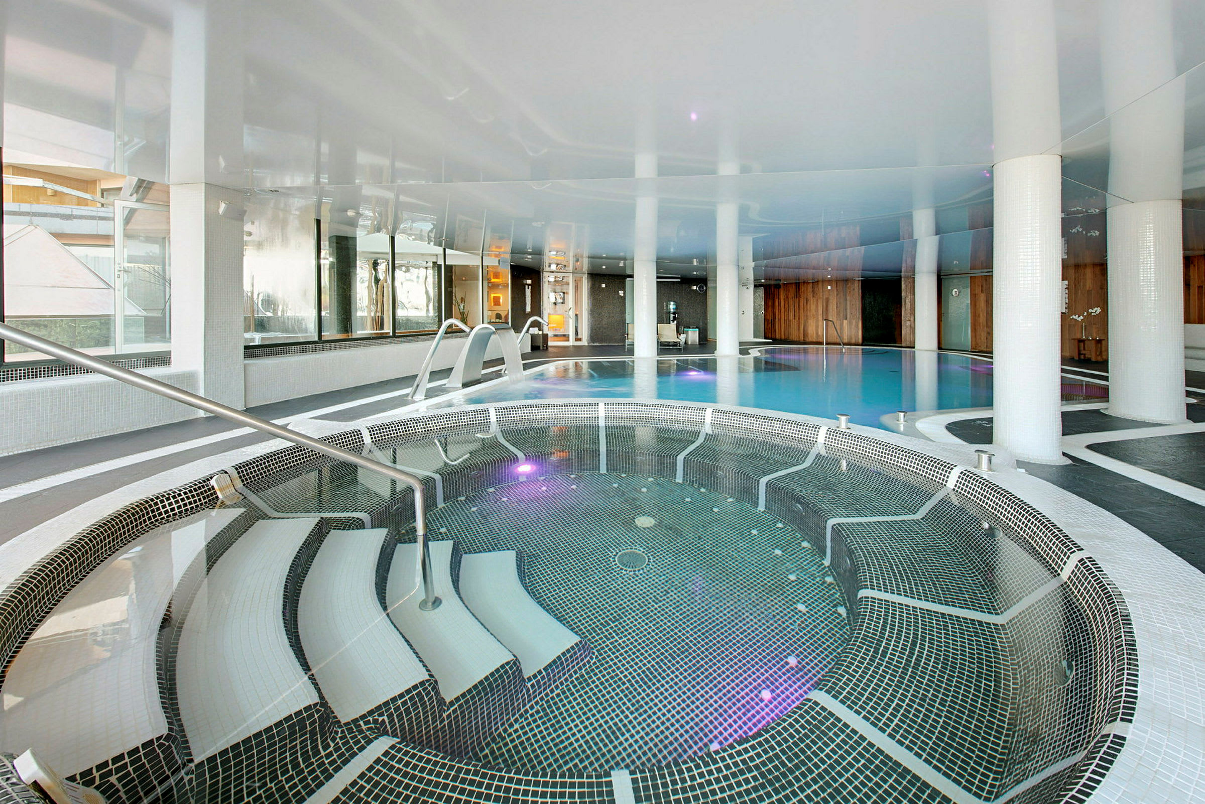 En indendørs pool med et boblebad i forgrunden og en større pool i baggrunden. (AI-genereret tekst)