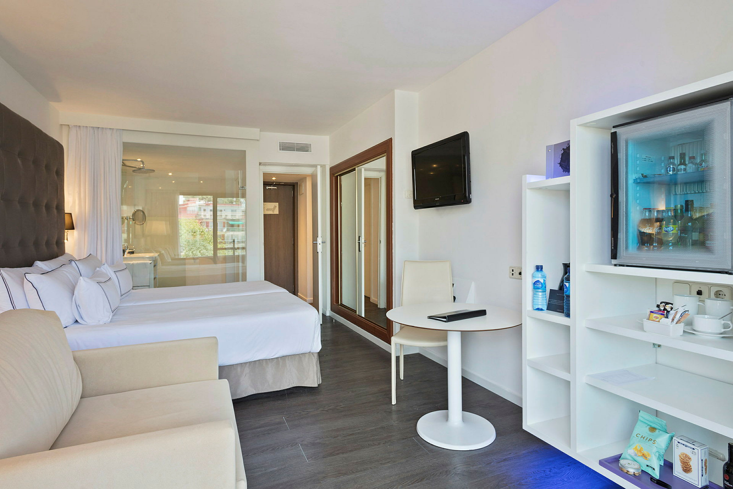 Hotelværelse med dobbeltseng, siddepladser, bord og en minibar. (AI-genereret tekst)