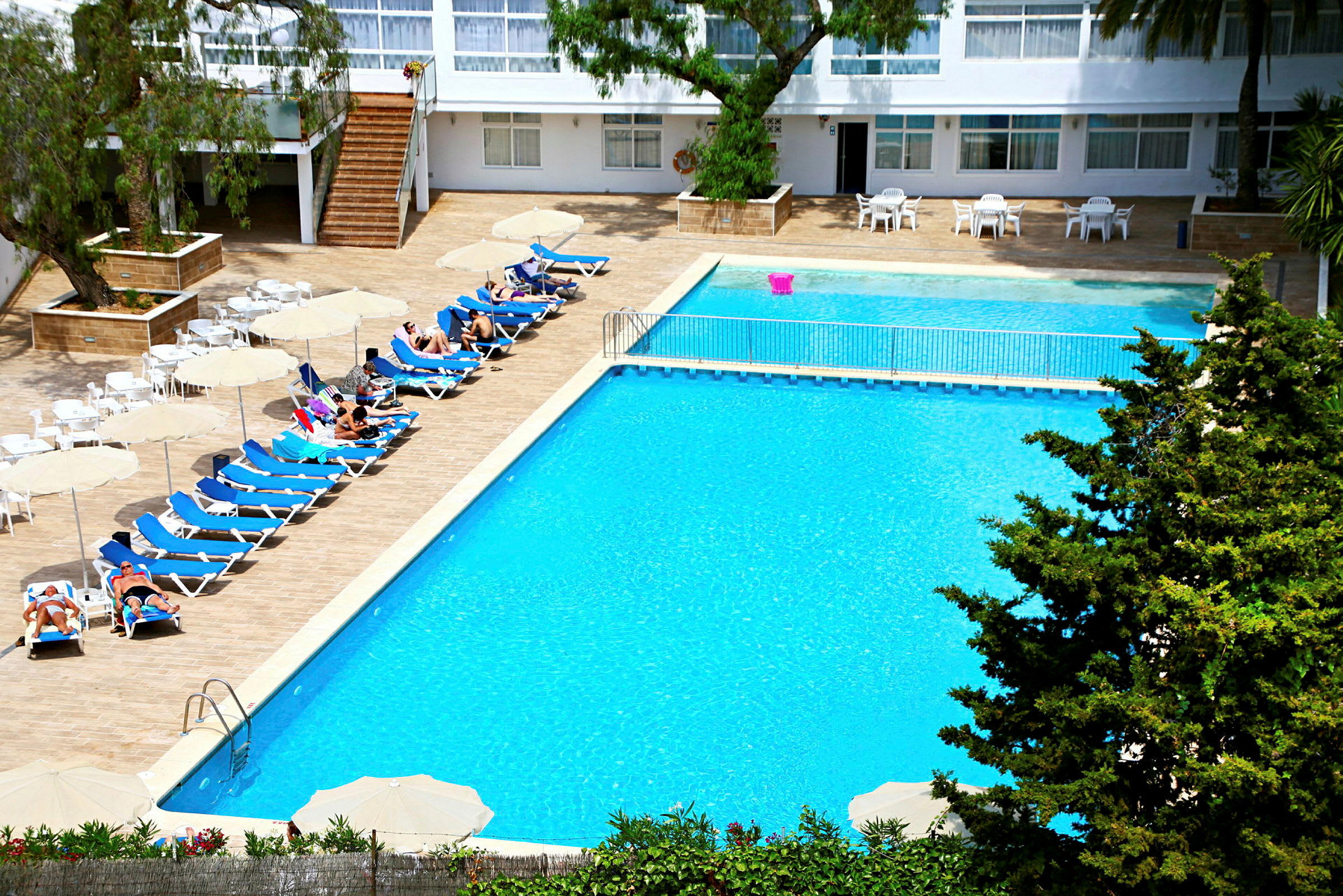 En hotelpool med liggestole, parasoller og mennesker, der nyder solen. (AI-genereret tekst)