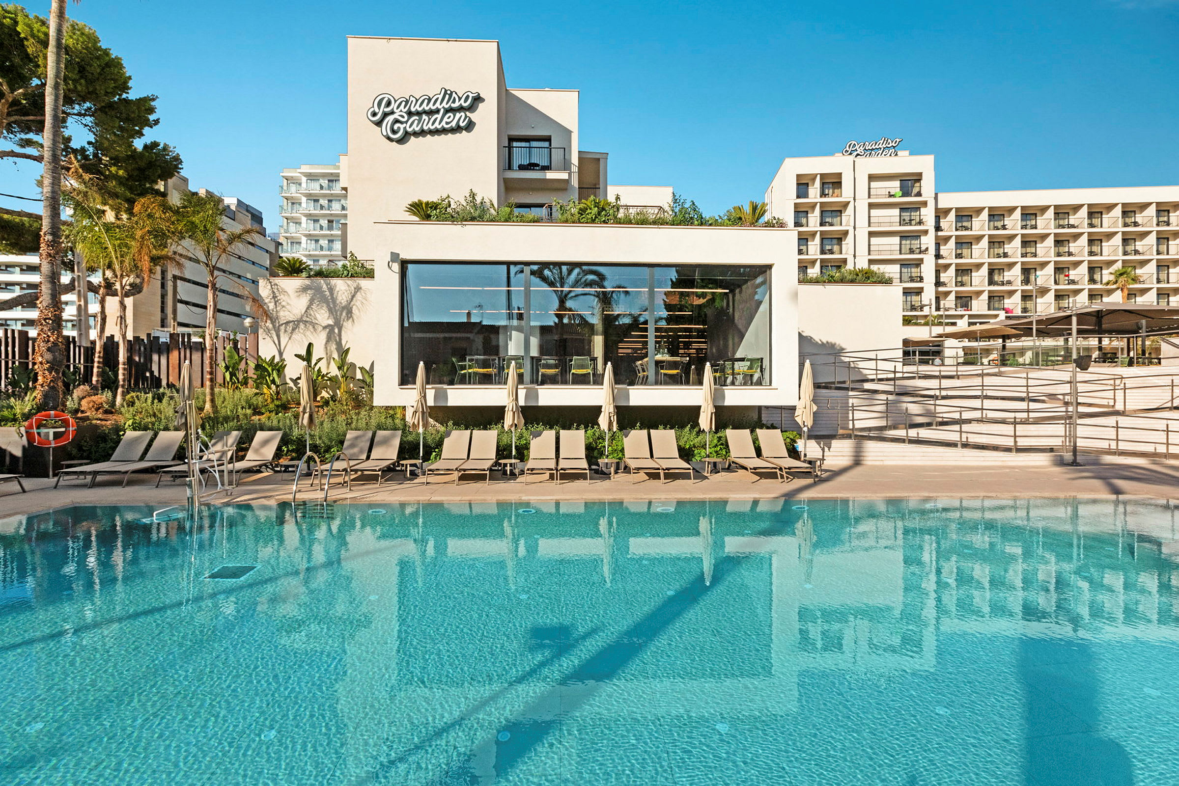 Billede af et hotel med en pool og liggestole foran bygningen Paradiso Garden. (AI-genereret tekst)