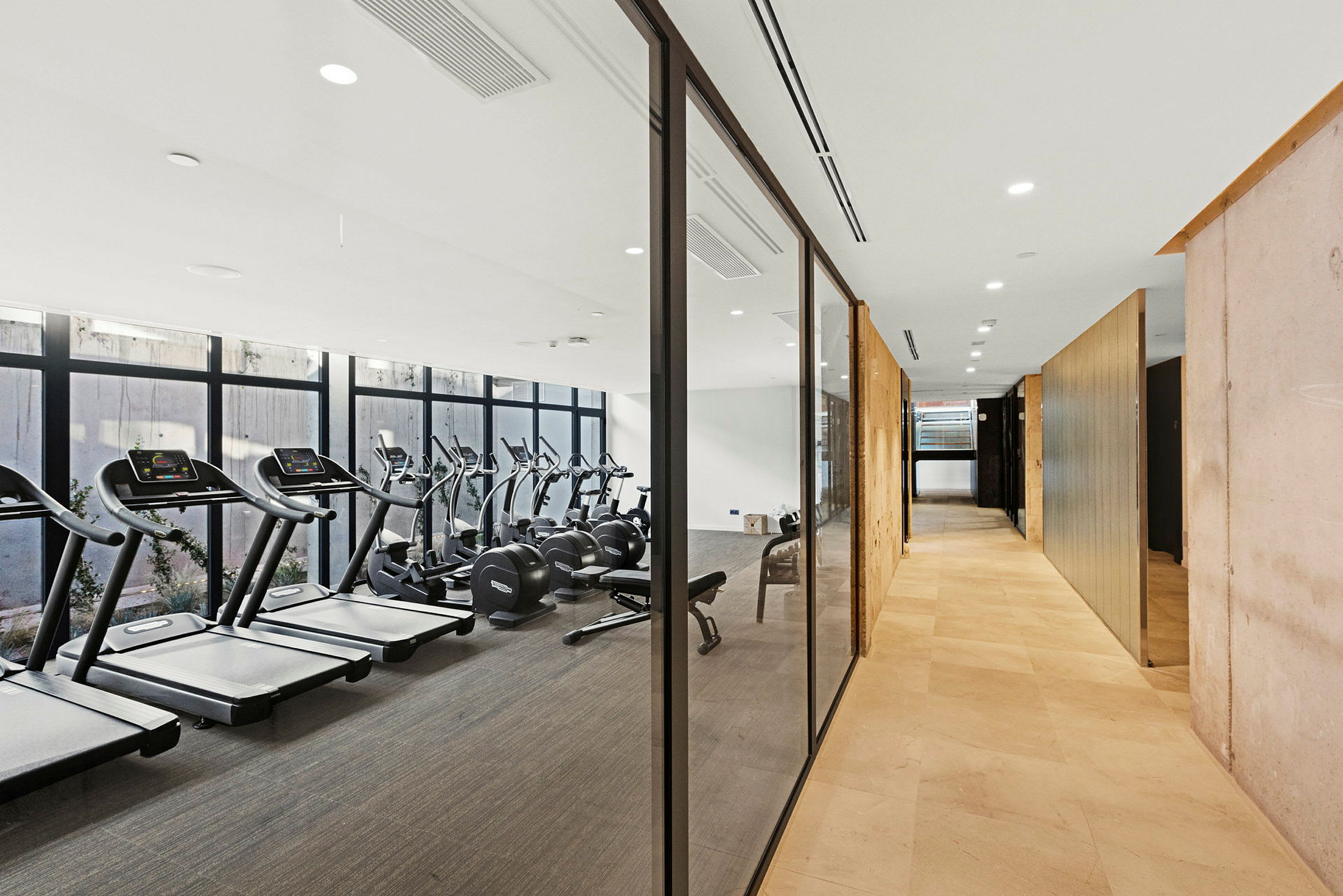 Billede af et fitnesscenter med glasvægge, der adskiller det fra en lys gang. (AI-genereret tekst)
