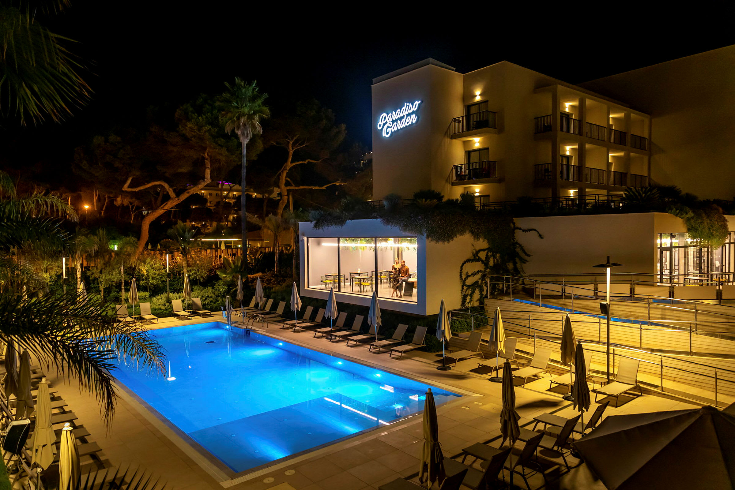 Hotel Paradiso Garden set om aftenen med en oplyst pool og liggestole i forgrunden. (AI-genereret tekst)