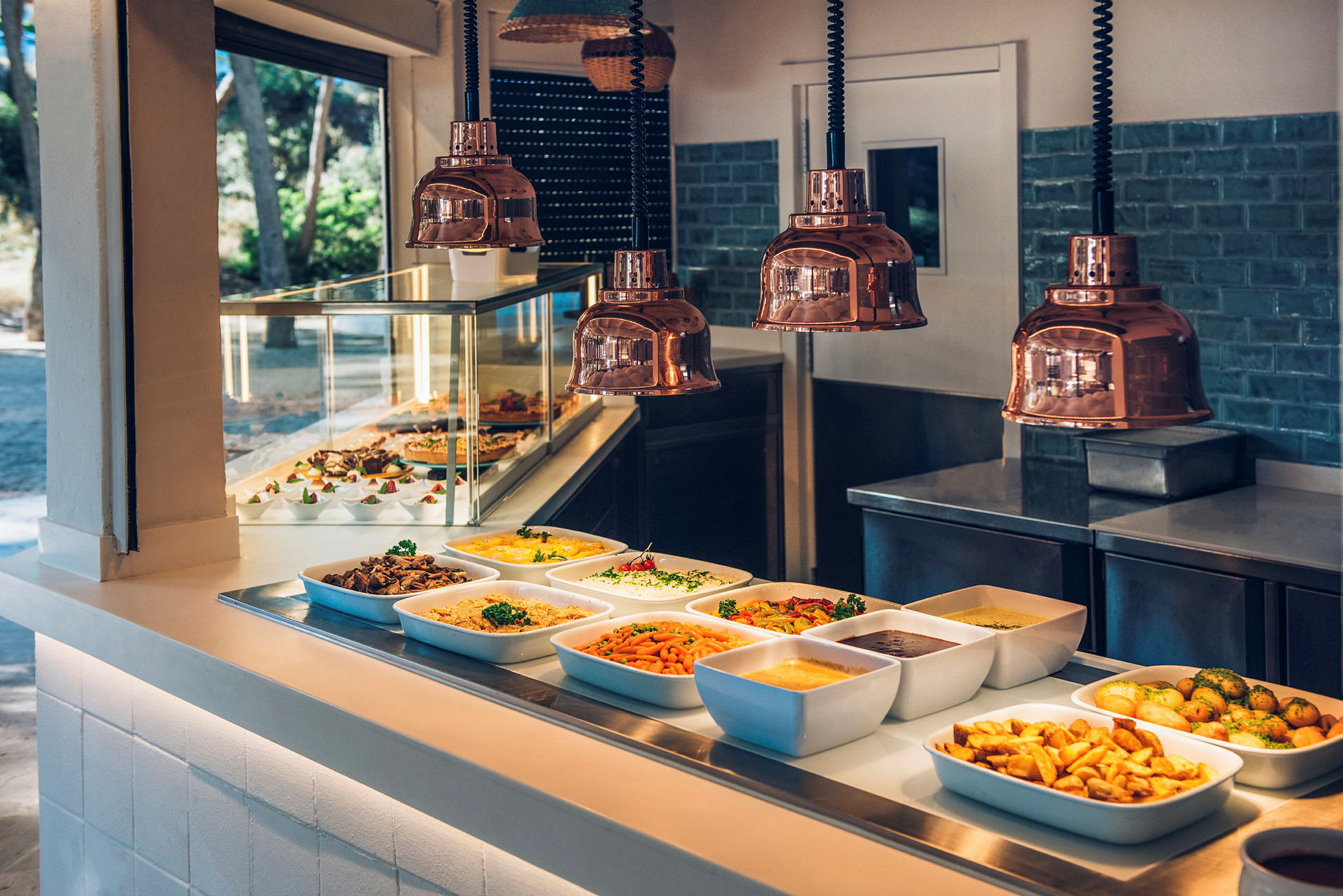 En buffet med flere retter serveret i hvide fade og skåle på en serveringsdisk. Kobberlamper ses ovenover. (AI-genereret tekst)