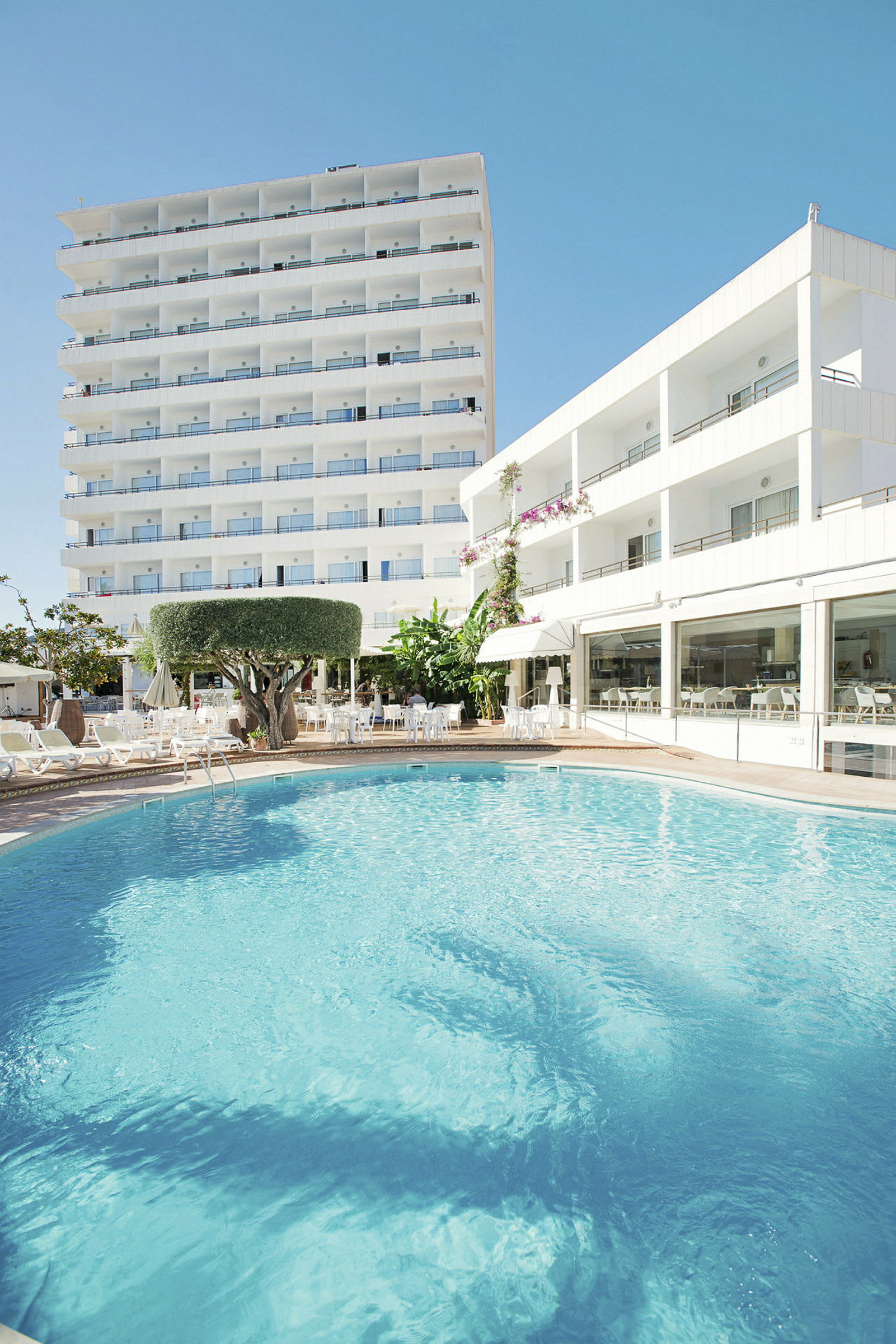 Hotelbygninger ses omkring en udendørs pool. (AI-genereret tekst)