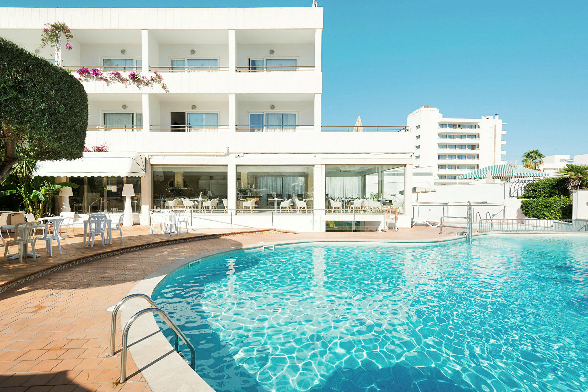 Hotelbygning med en udendørs swimmingpool i forgrunden. (AI-genereret tekst)