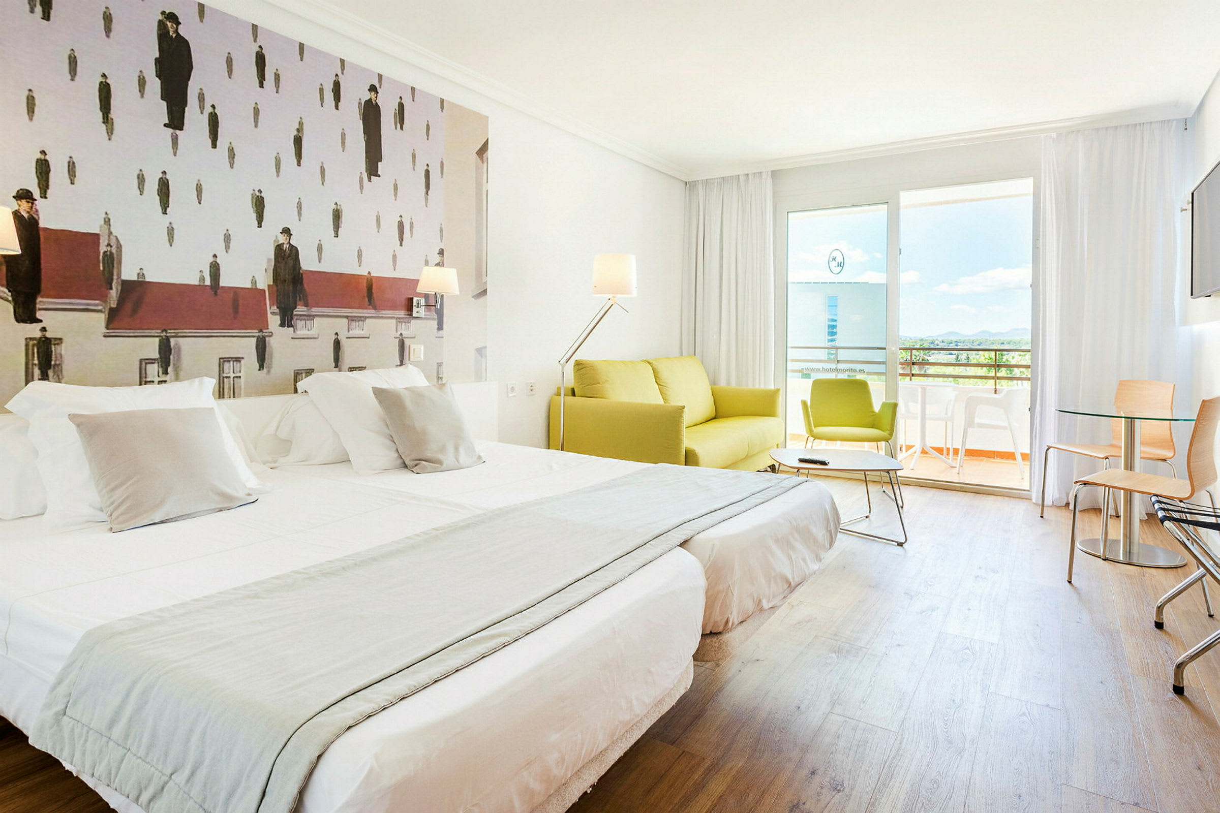 Et hotelværelse med to opdækkede enkeltsenge, en grøn sofa og en balkon i baggrunden. Væggudsmykningen har et kunstværk med et usædvanligt design. (AI-genereret tekst)