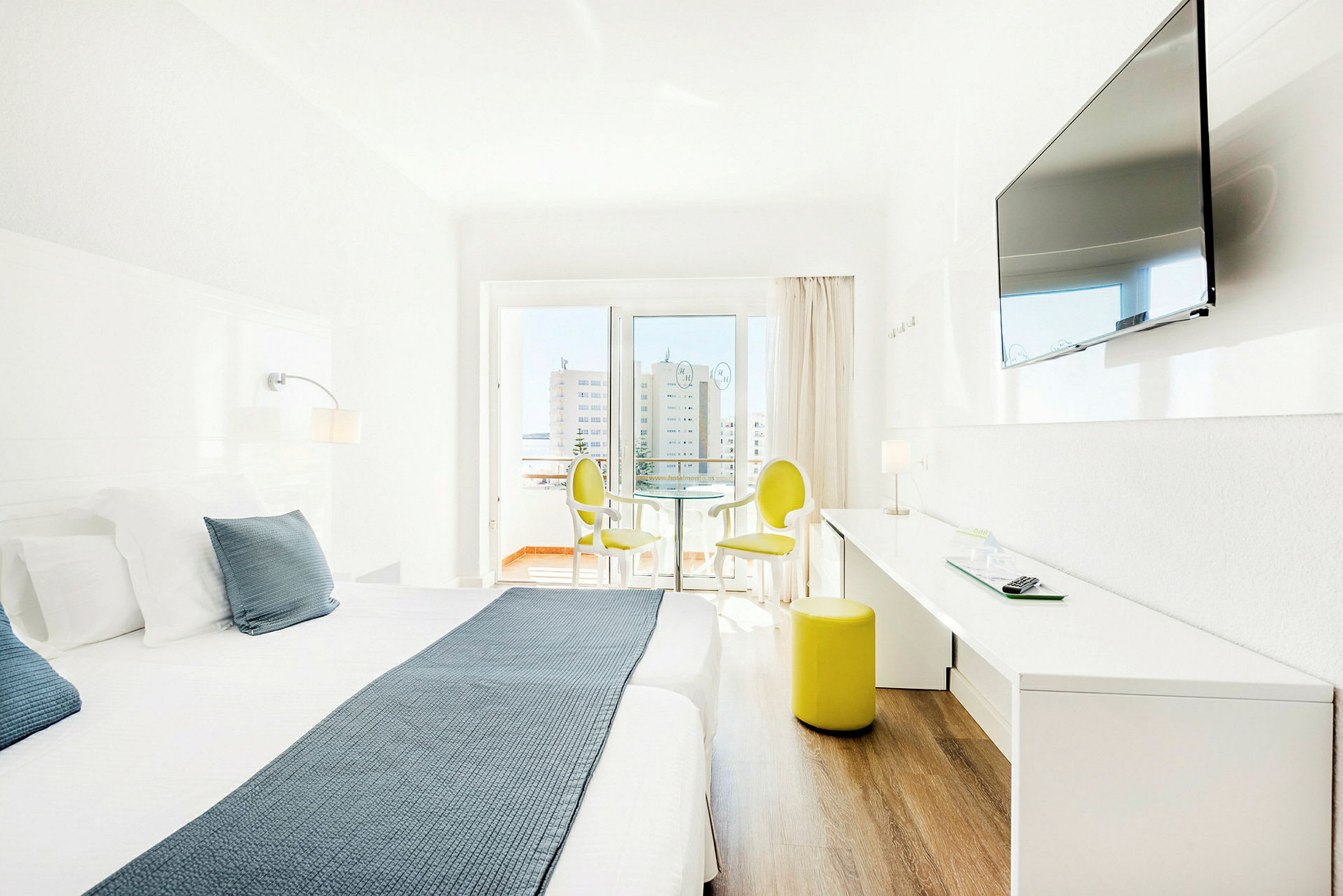 Lyst hotelværelse med dobbeltseng, TV på væggen og siddepladser ved vinduet. (AI-genereret tekst)