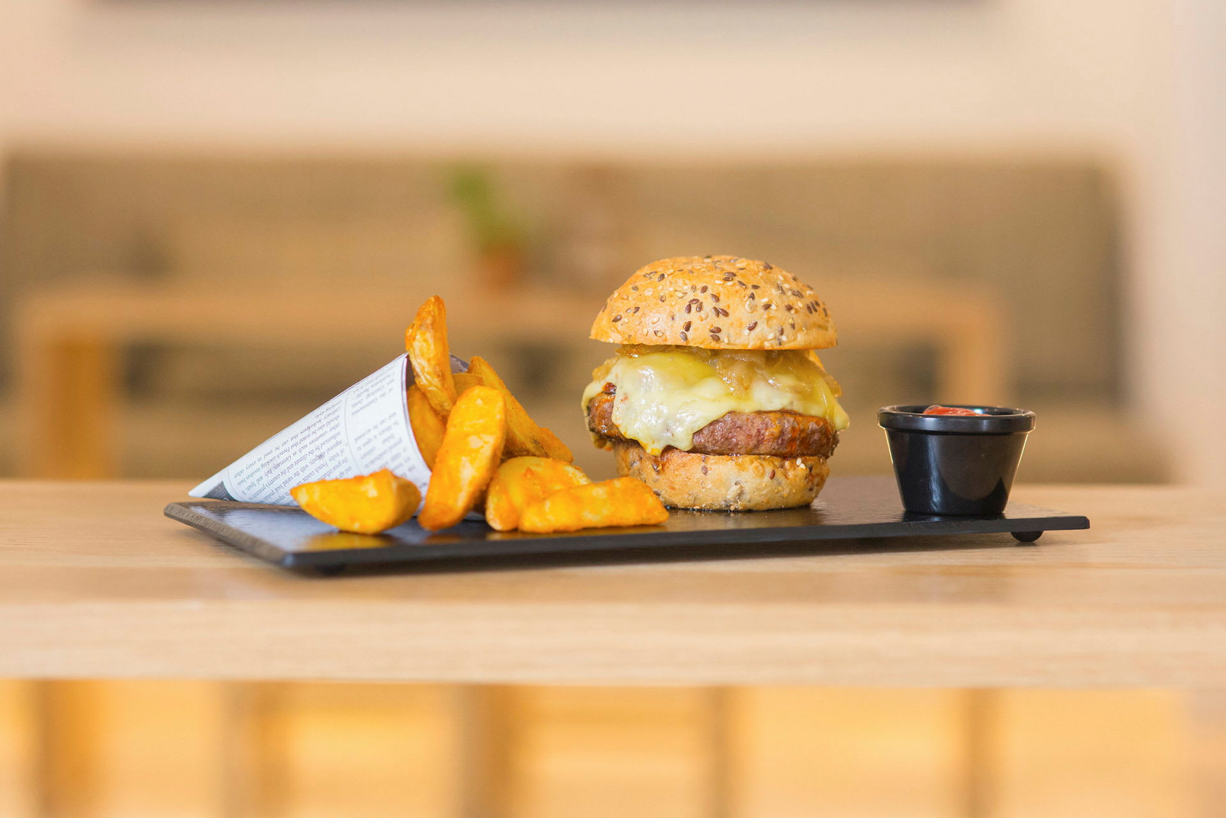 Burger med ost, kartoffelbåde og dip på en tallerken. (AI-genereret tekst)