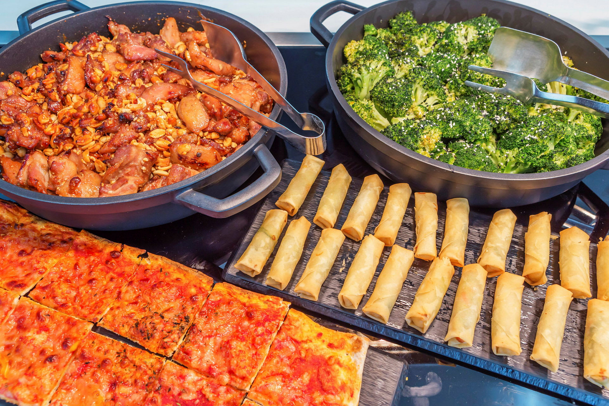 En buffet med forskellige retter, herunder kylling, broccoli, forårsruller og pizza. (AI-genereret tekst)