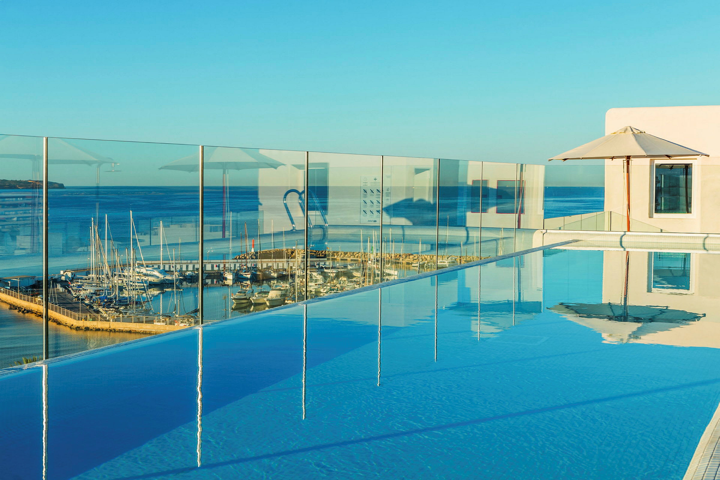 En pool med glasrækværk og udsigt over en havn med både ved havet. (AI-genereret tekst)