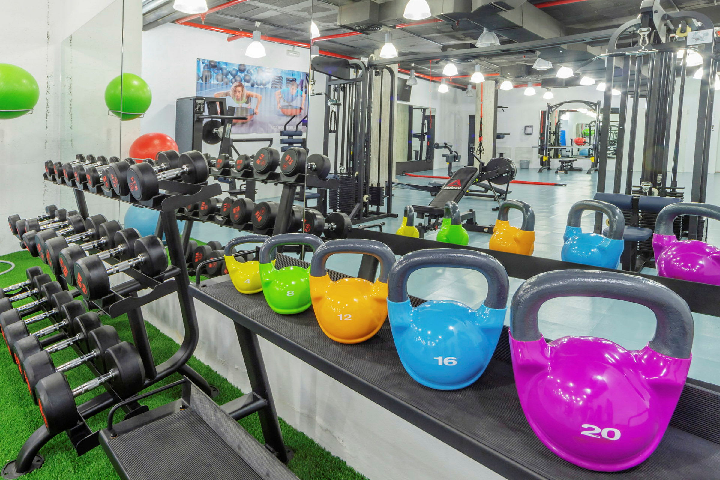 Billede af et træningscenter med håndvægte på en reol og kettlebells i forskellige farver placeret på en hylde, med træningsudstyr i baggrunden. (AI-genereret tekst)