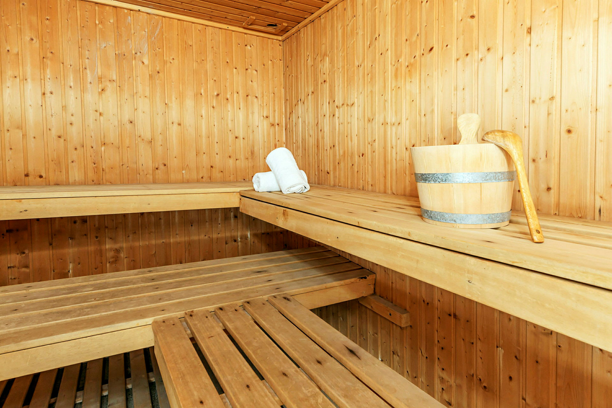 En sauna beklædt med træpaneler, træbænke, en træspand med en øse samt to sammenrullede hvide håndklæder. (AI-genereret tekst)