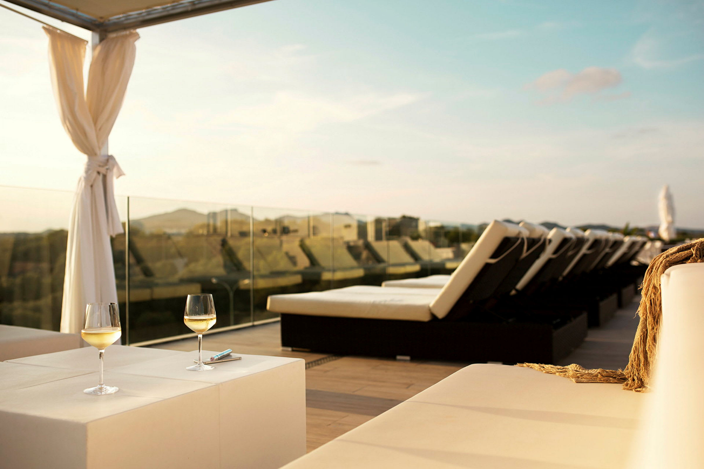 Solterrasse med liggestole, to glas hvidvin på et bord og udsigt over landskabet. (AI-genereret tekst)