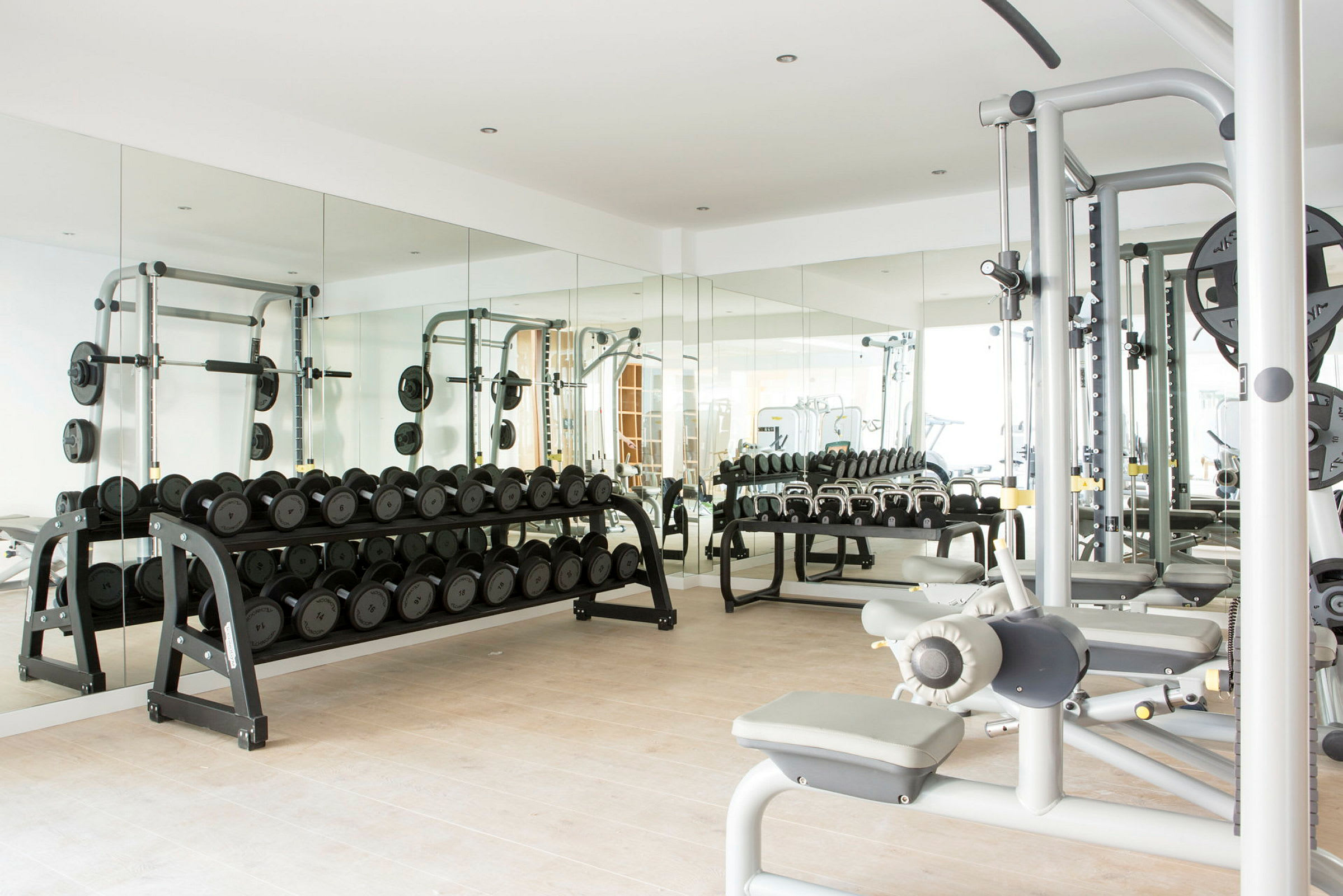 Et fitnesscenter med håndvægte, træningsmaskiner og spejle. (AI-genereret tekst)