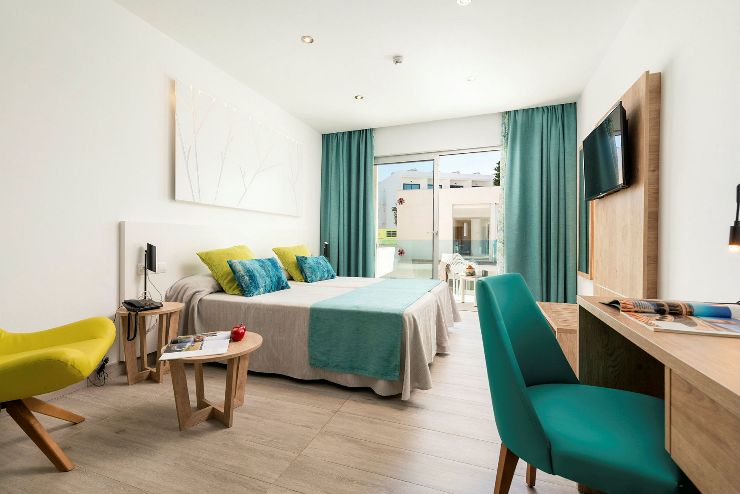 Et moderne hotelværelse med en dobbeltseng dækket med skarpe tekstiler, siddepladser og et skrivebord. Vinduer fører til en altan. (AI-genereret tekst)