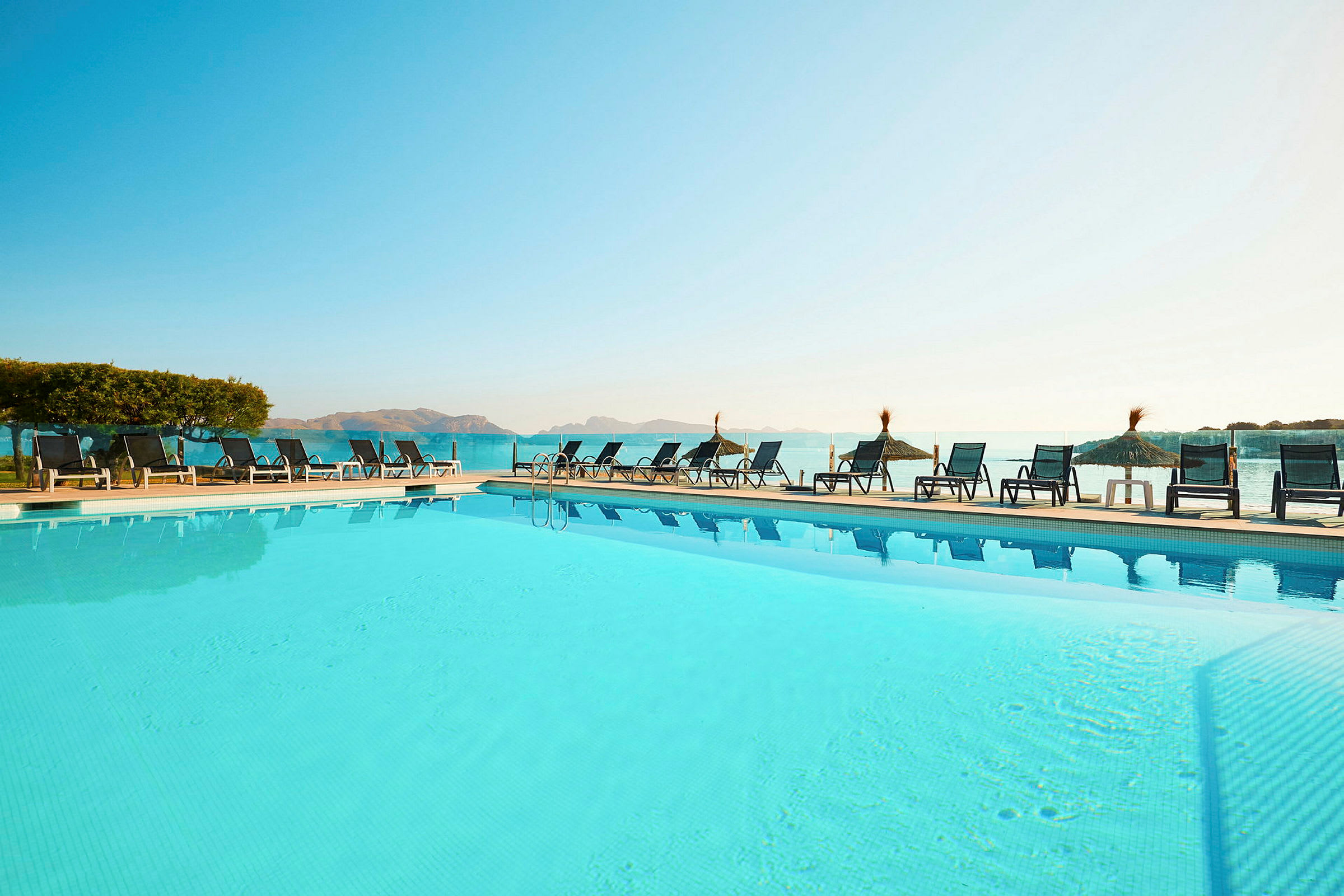 Hotelpool med liggestole og parasoller med havudsigt. (AI-genereret tekst)