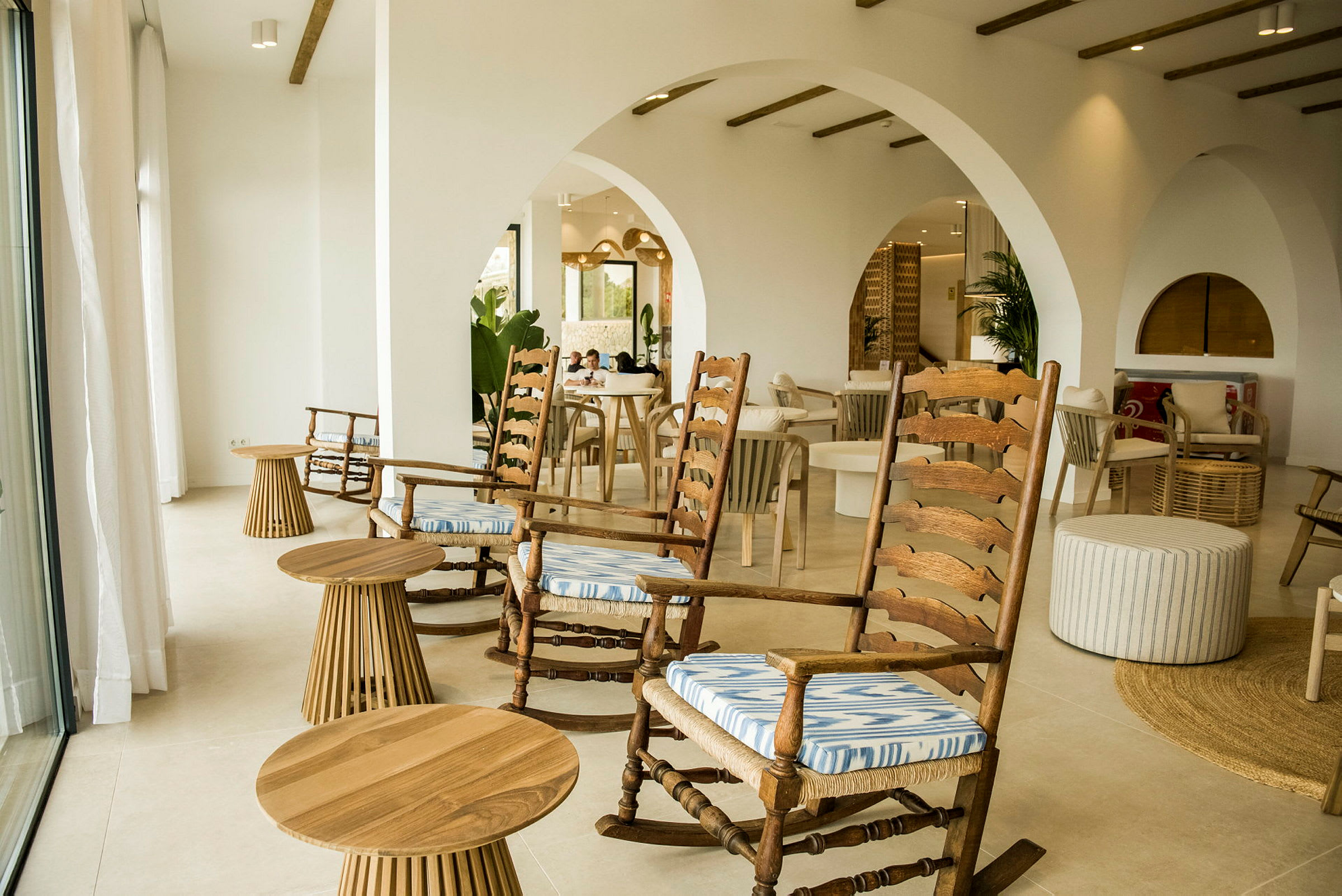 Et lyst indendørsmiljø med trægyngestole og små runde borde. (AI-genereret tekst)