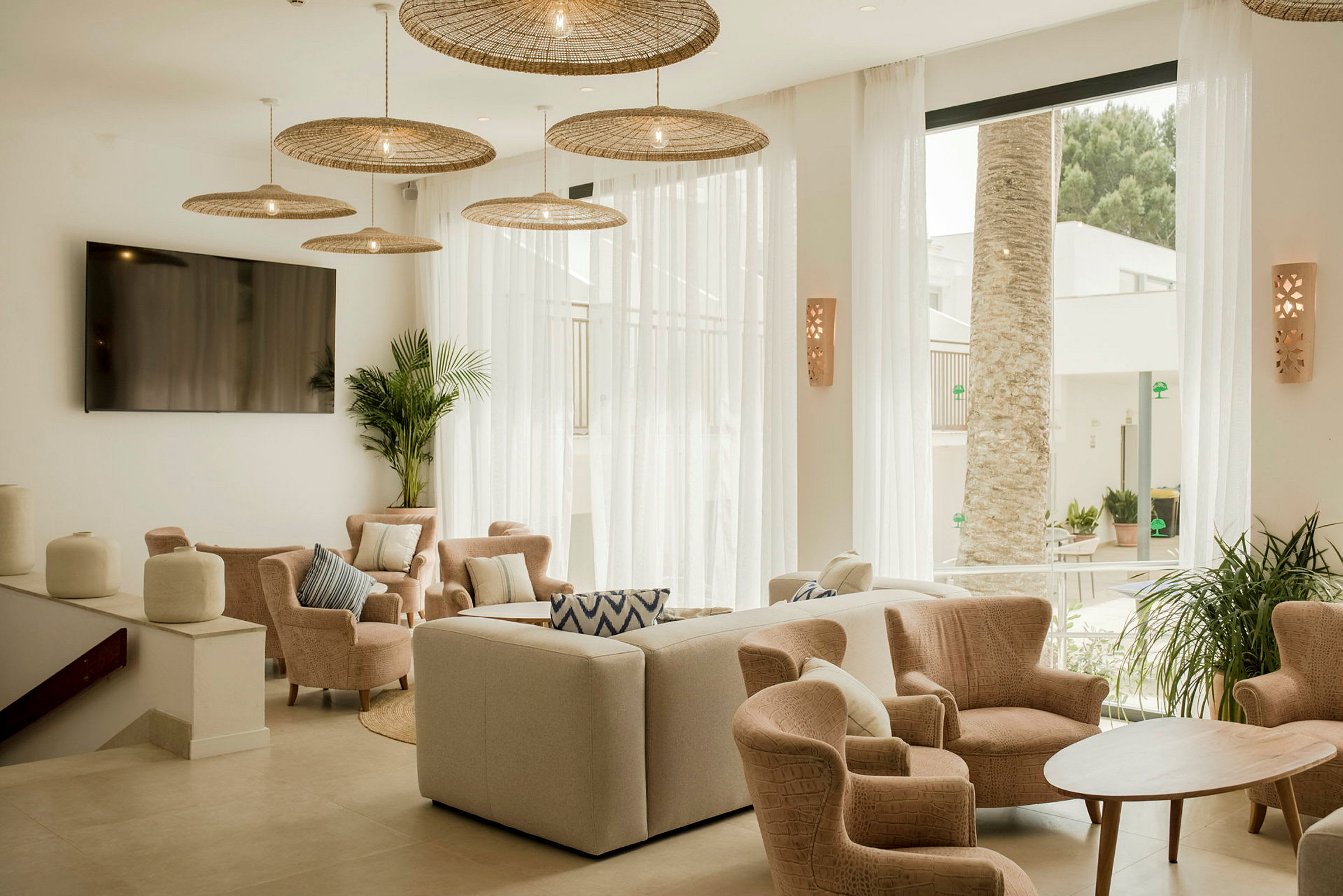 En lys og elegant dagligstue med stole og sofa rundt om et træbord samt store vinduer med udsigt til palmer udenfor. (AI-genereret tekst)