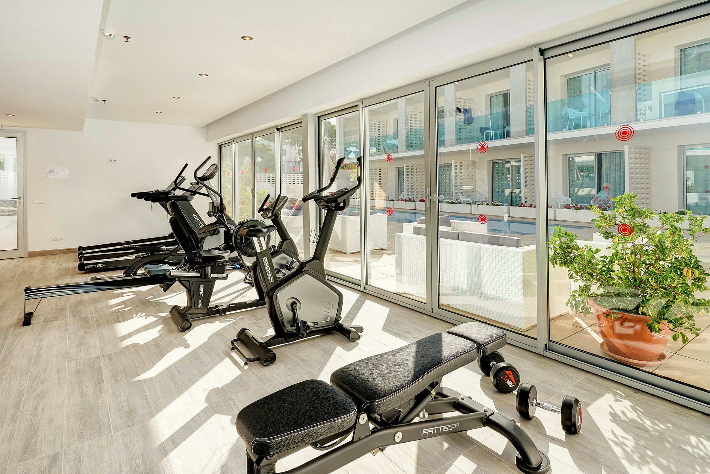 Fitnesscenter med træningsudstyr og store vinduer, der vender ud mod en terrasse. (AI-genereret tekst)