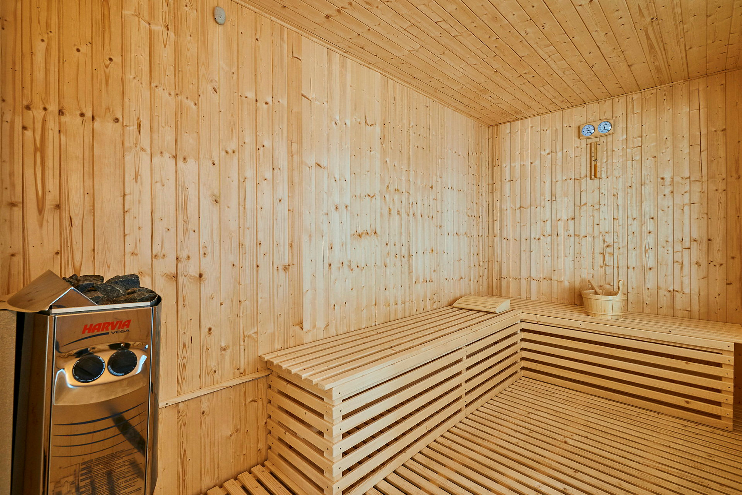 Interiør i en sauna med træpaneler på vægge og bænke samt en Harvia-enhed. (AI-genereret tekst)