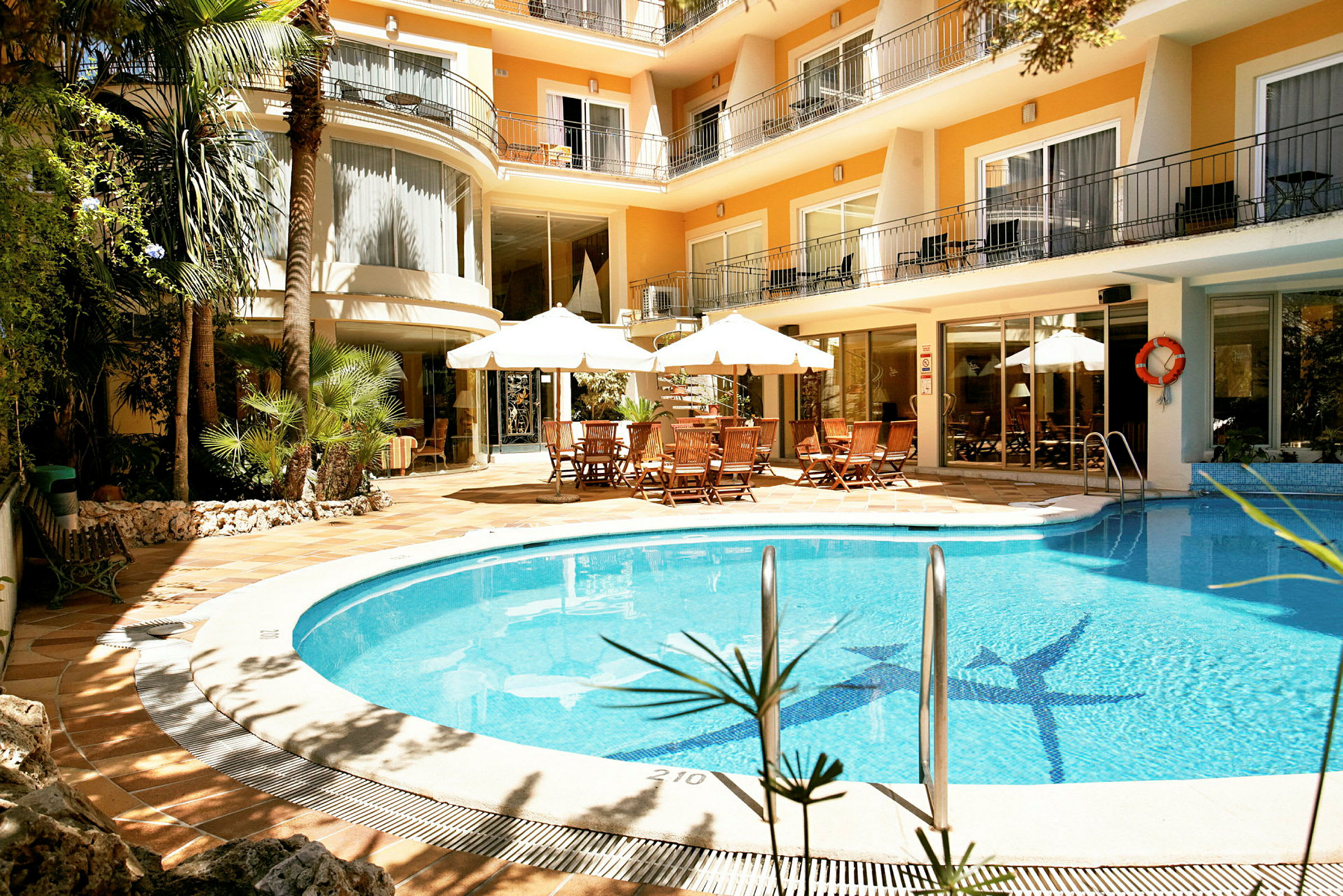 Et hotel med en udendørs pool, liggestole og borde under parasoller. (AI-genereret tekst)