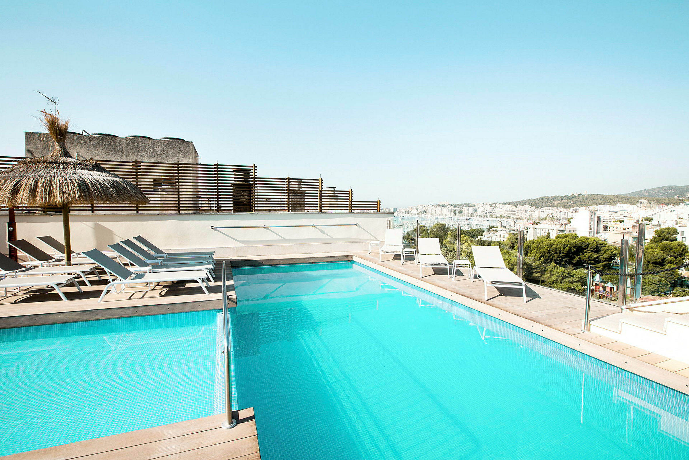 En swimmingpool på en terrasse med liggestole og udsigt over en by. (AI-genereret tekst)
