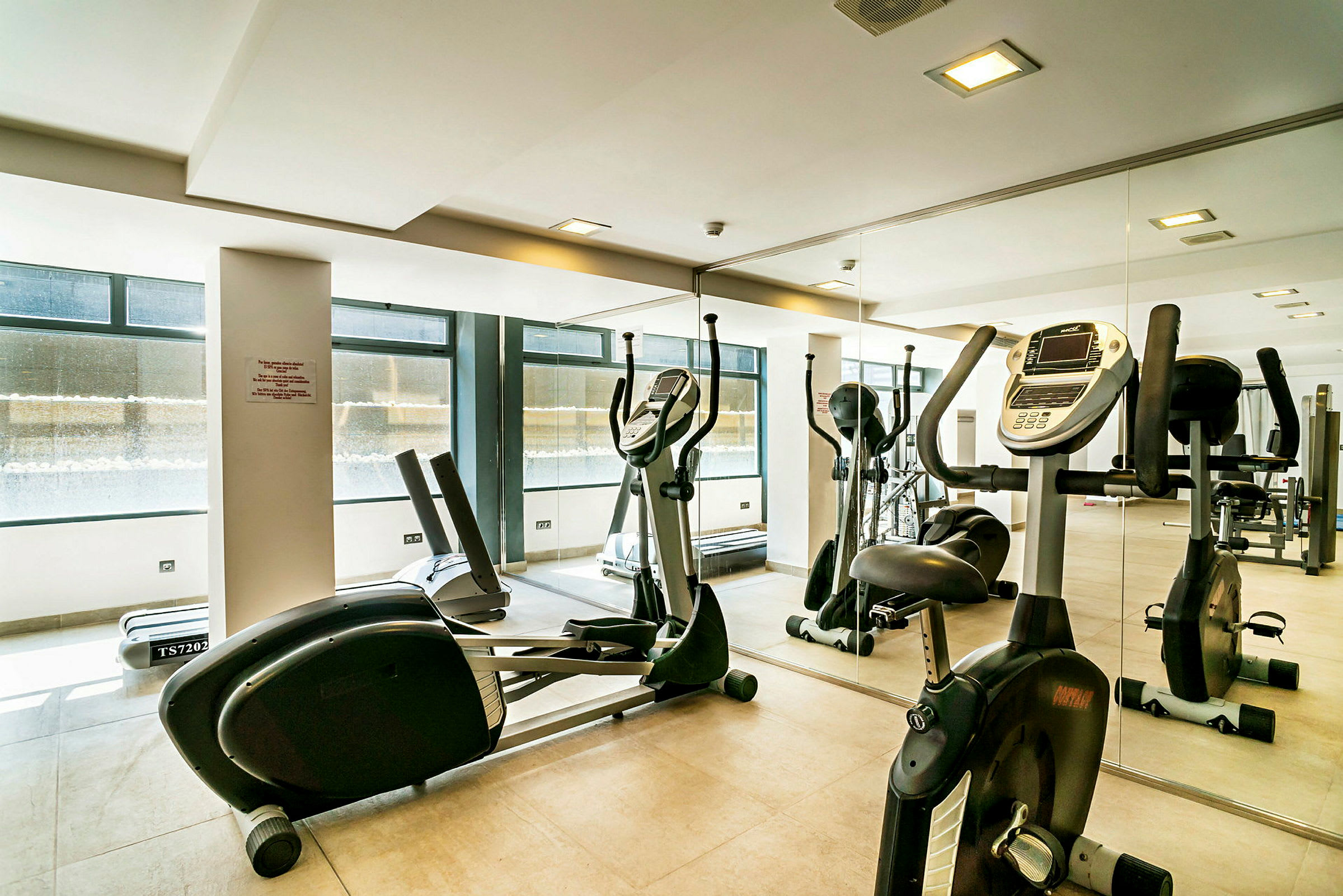 Fitnessrum med motionscykler og træningsudstyr foran et spejl. (AI-genereret tekst)