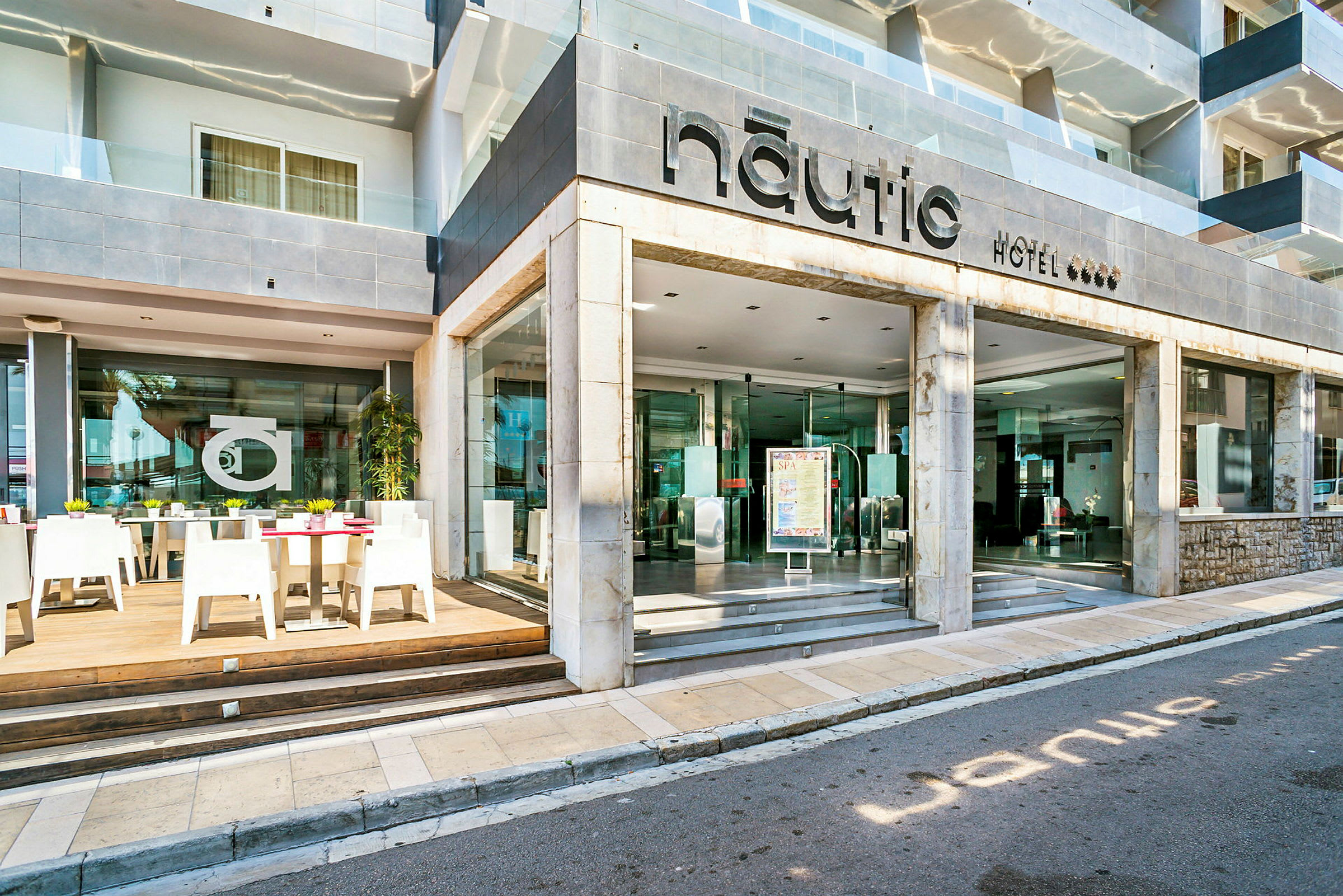 Hotel Nautic indgang og udendørs servering med borde og stole. (AI-genereret tekst)