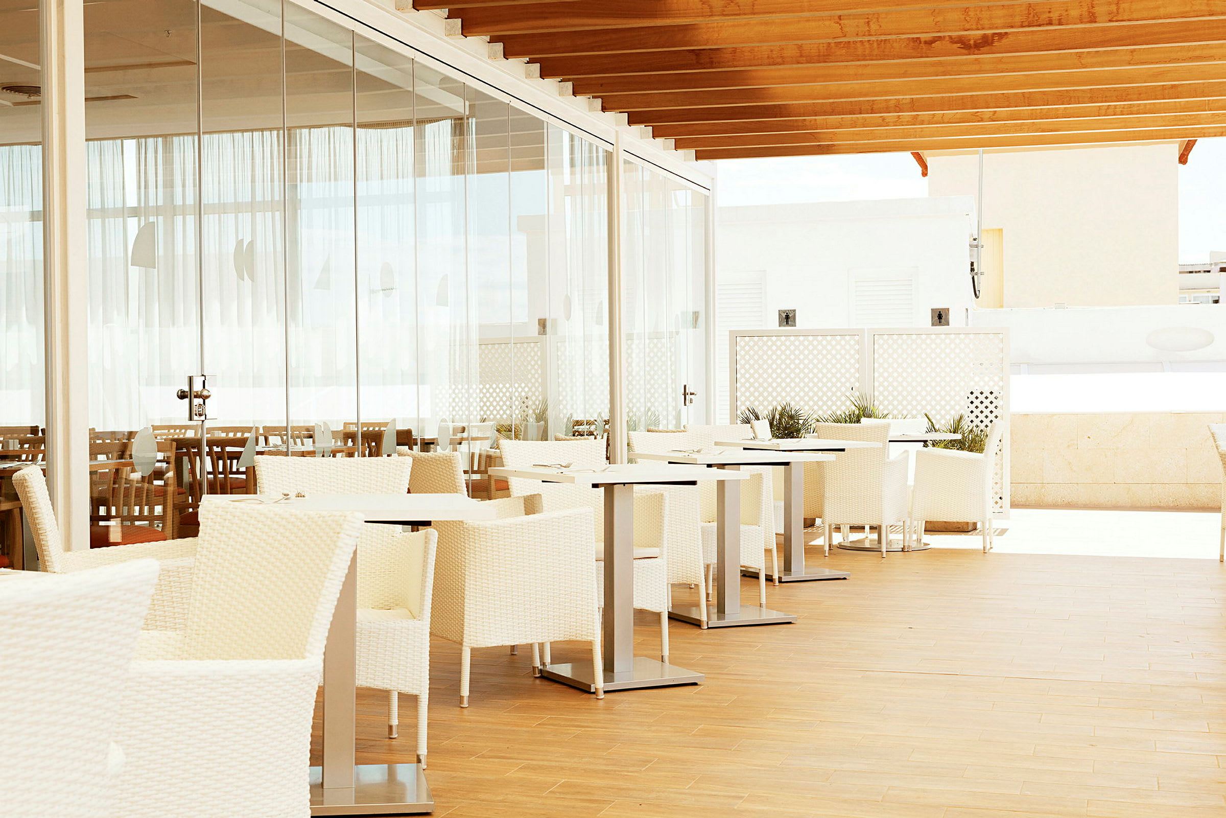 Udendørs restaurant med hvide møbler og glasvæg. (AI-genereret tekst)