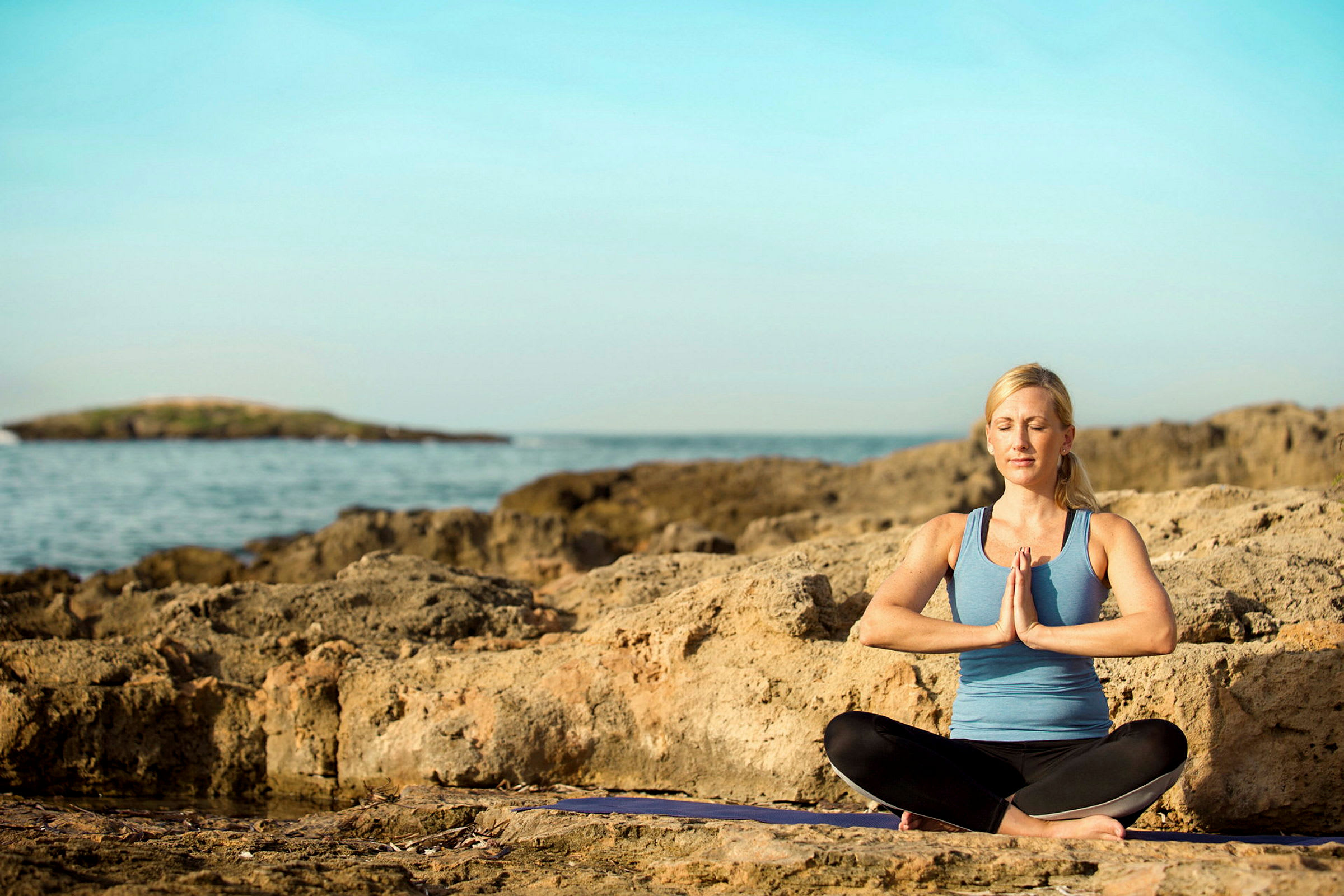 Person i træningstøj sidder i meditationsstilling på en klippe ved havet. (AI-genereret tekst)
