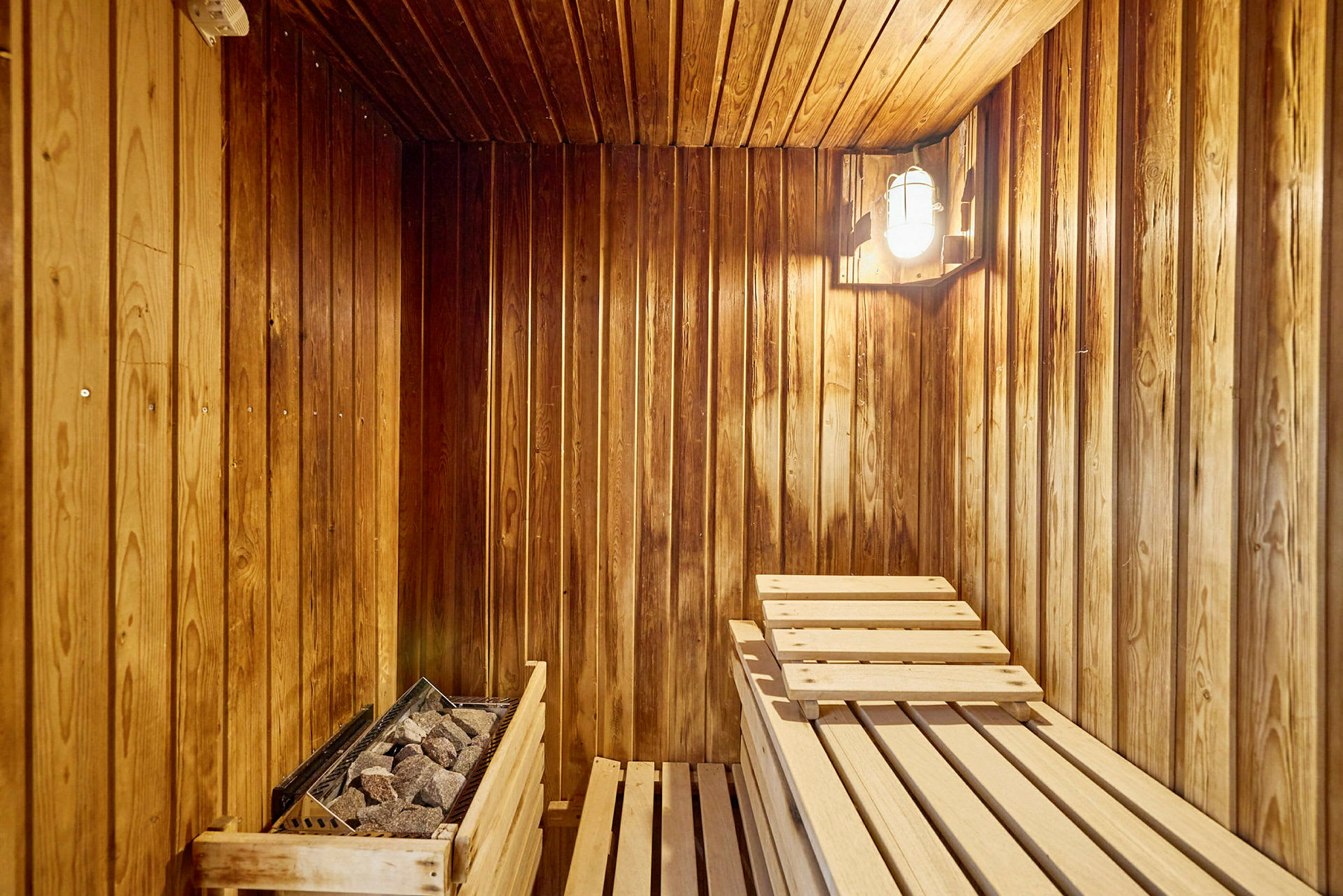 En træbeklædt sauna med træbænke og en stenovn. (AI-genereret tekst)
