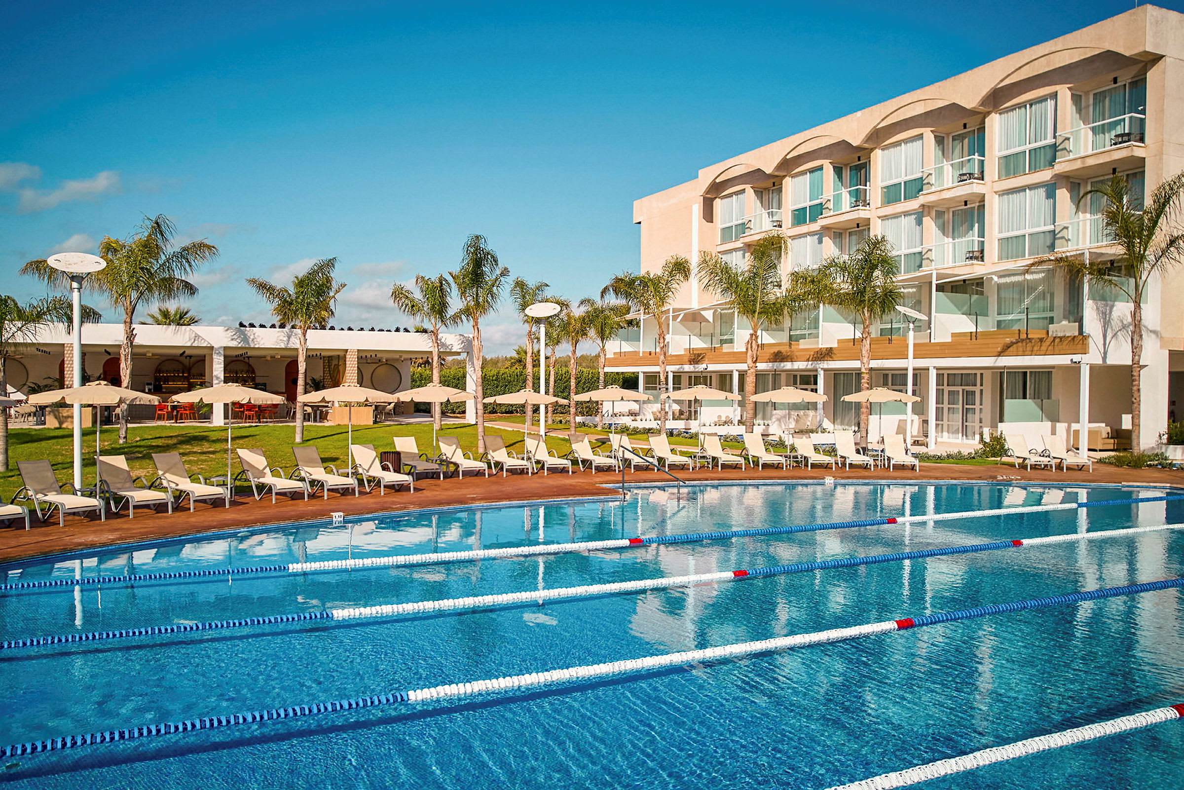 Hotel med pool og liggestole i forgrunden. (AI-genereret tekst)