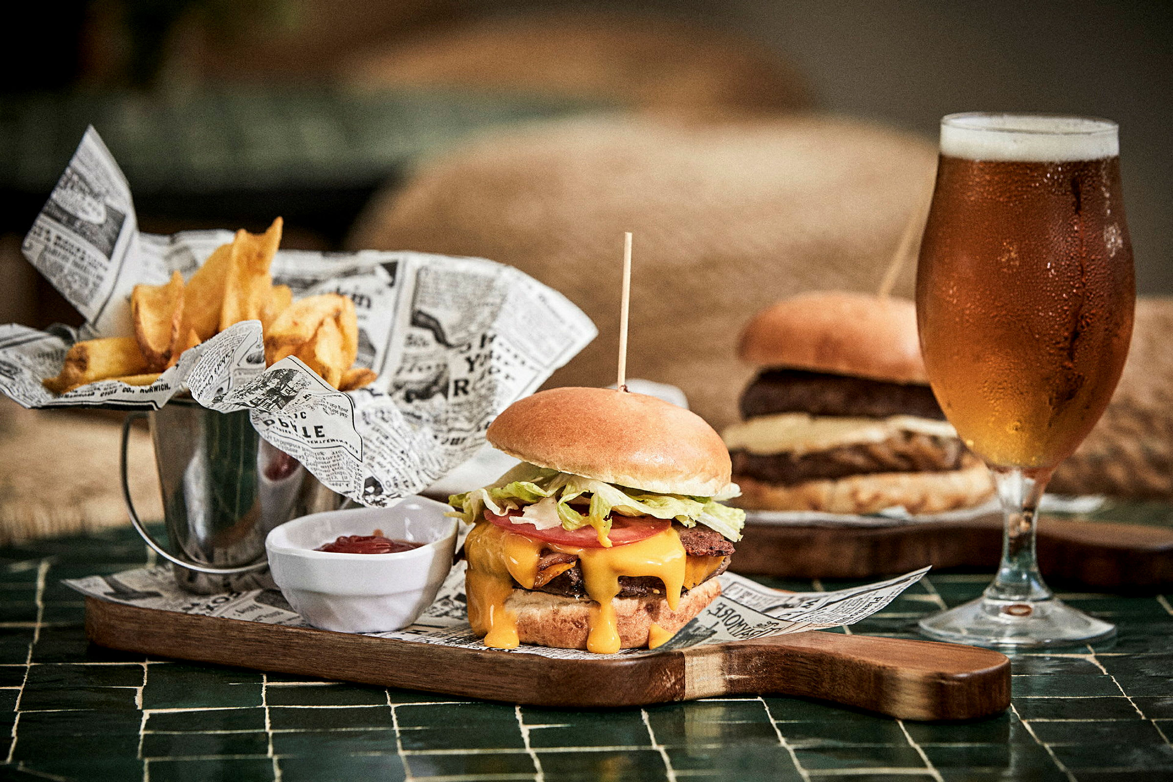 En burger, pommes frites og et glas øl på et bord. (AI-genereret tekst)