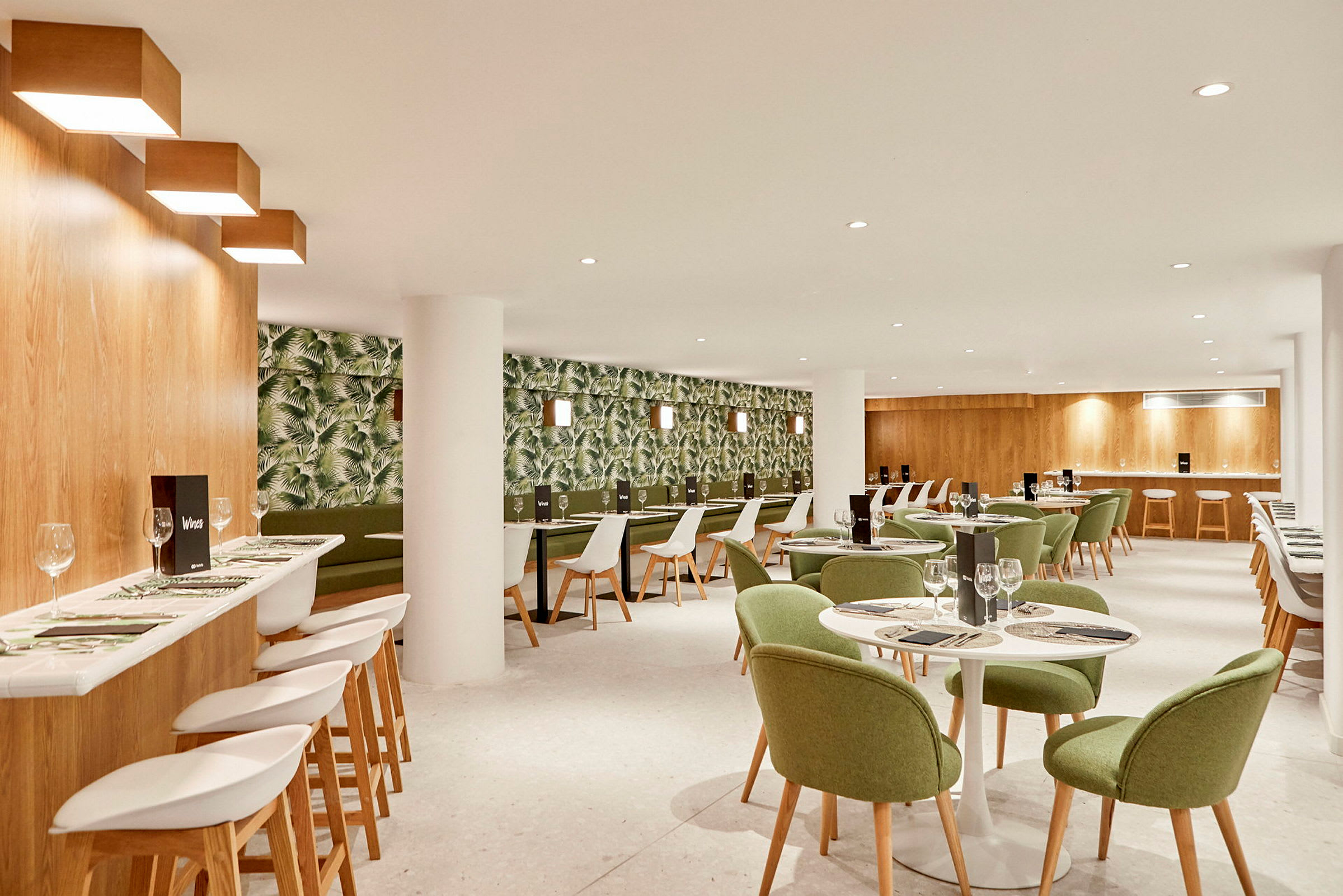 En restaurantinteriør med grønmalede stole og en tapetseret væg med plantemønster. (AI-genereret tekst)