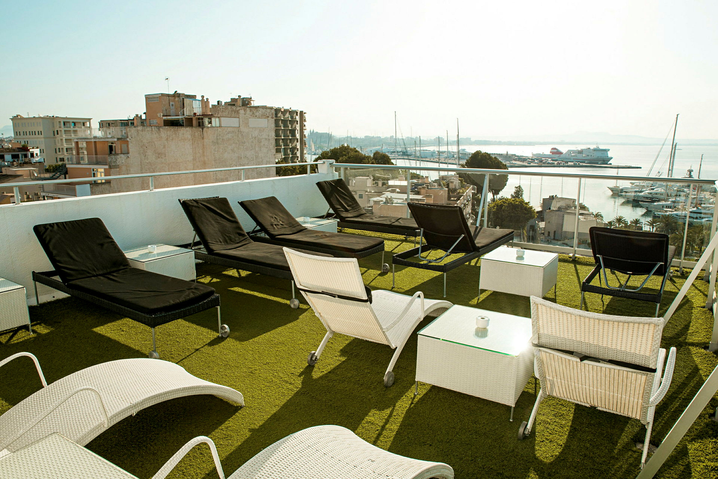 Udendørsområde med liggestole og borde på en terrasse med udsigt over en havn. (AI-genereret tekst)
