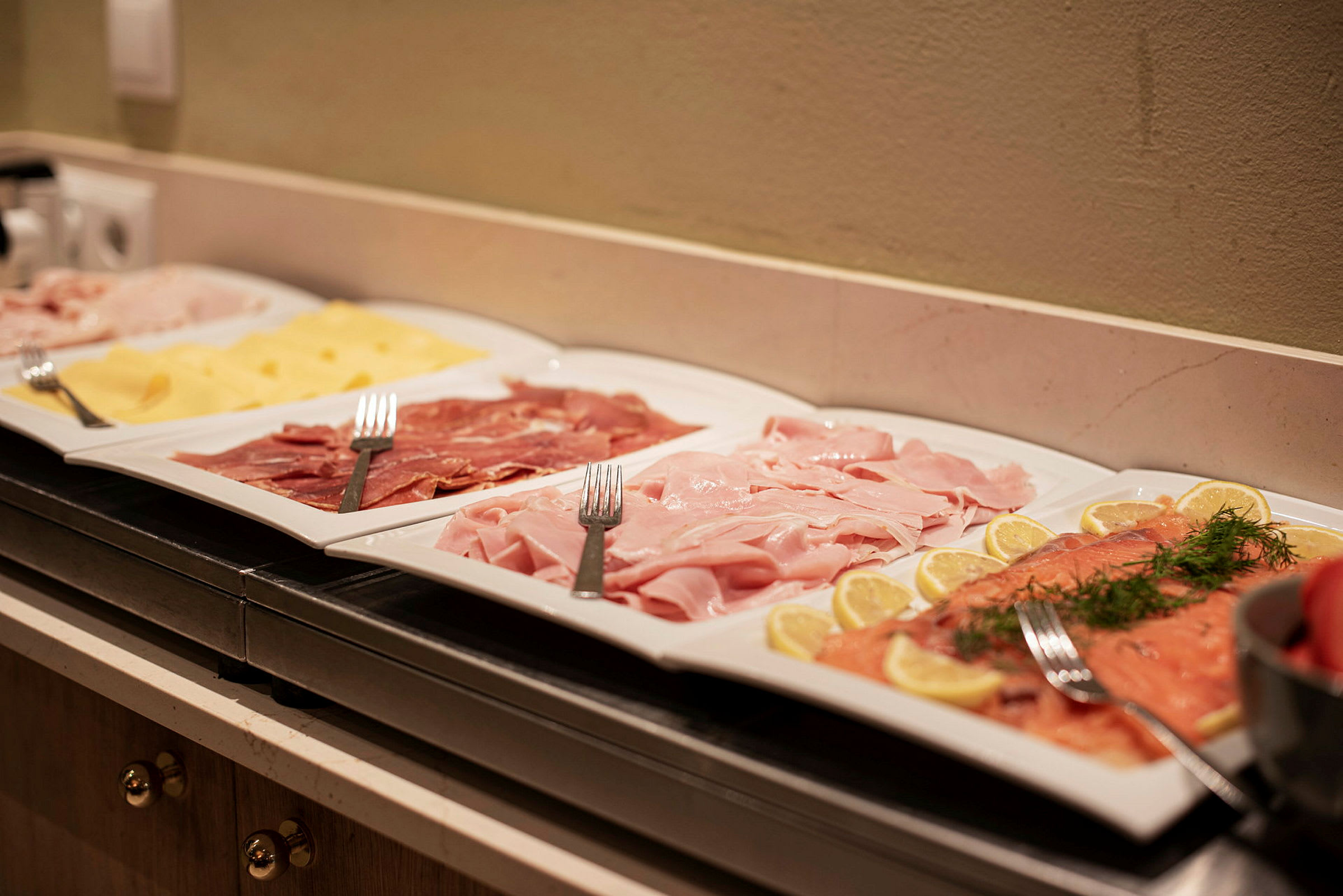 Fade med forskellige pålæg og ost arrangeret på en buffet. (AI-genereret tekst)