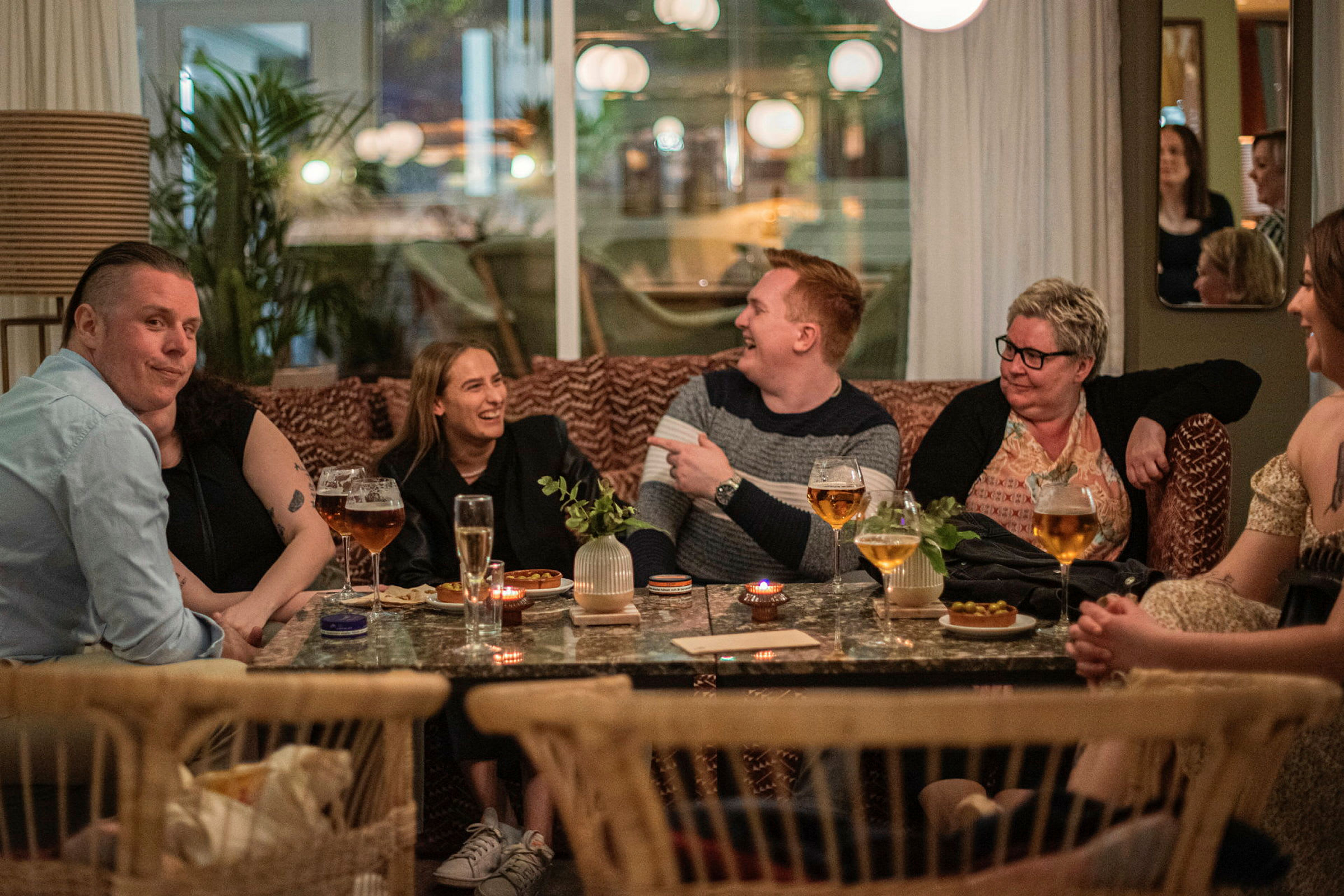 Folk sidder ved et bord med drikkevarer og snacks på en restaurant. (AI-genereret tekst)