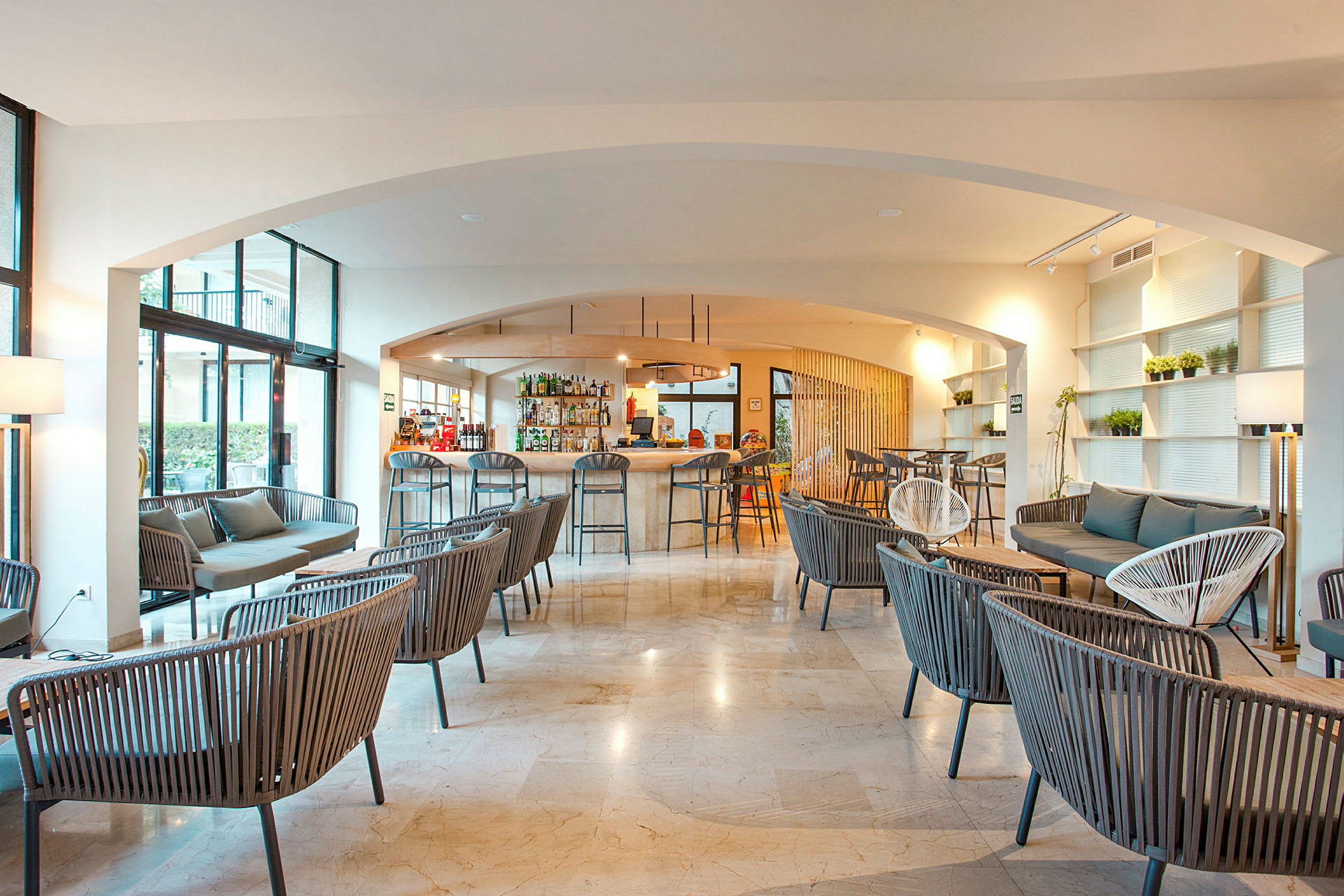 Interiør af en moderne lounge med bar, hvor flere siddegrupper er opstillet med stole og sofaer i et lyst og luftigt rum. (AI-genereret tekst)
