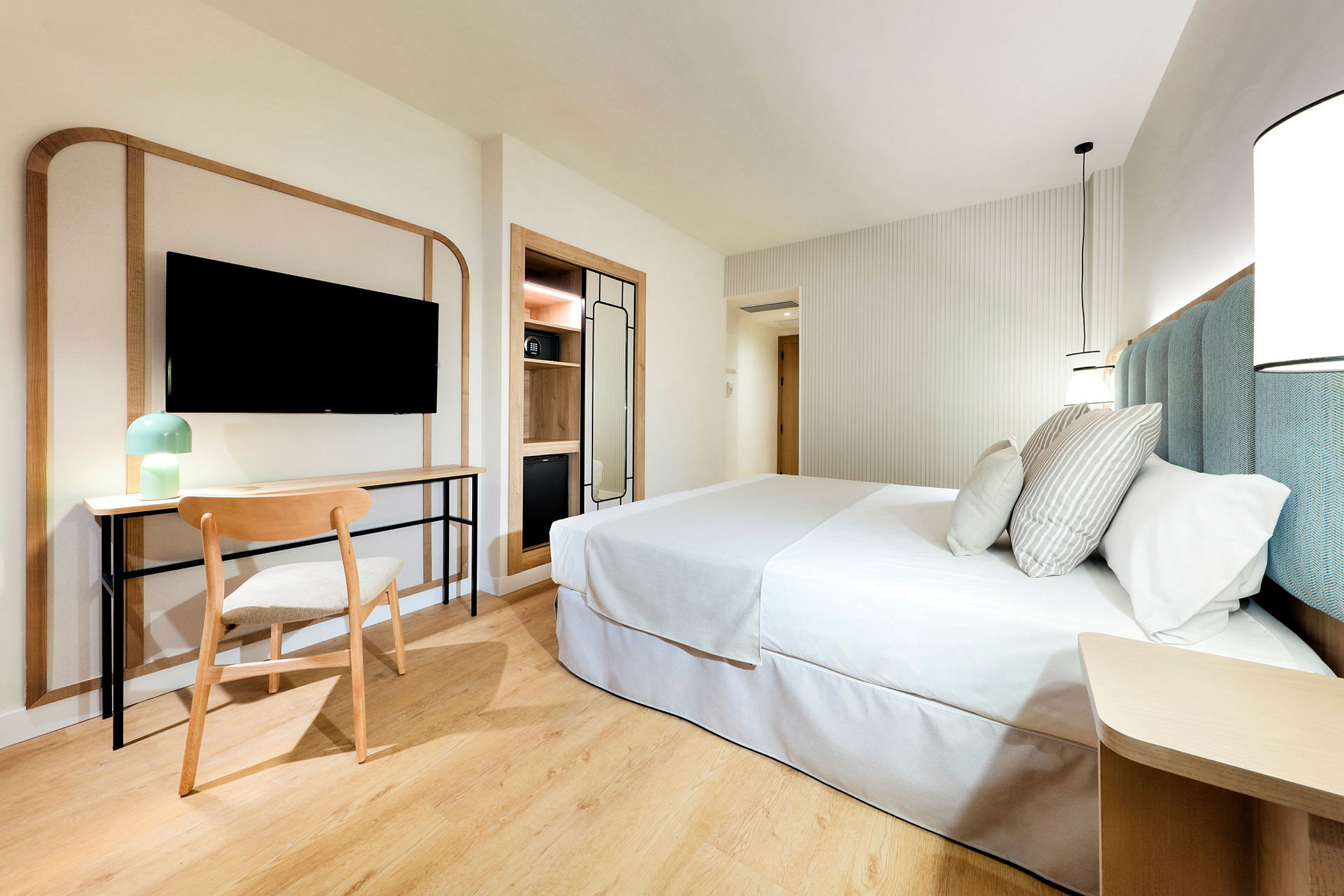 Et moderne og lyst hotelværelse med en dobbeltseng, skrivebord og stol samt et vægmonteret fjernsyn. (AI-genereret tekst)