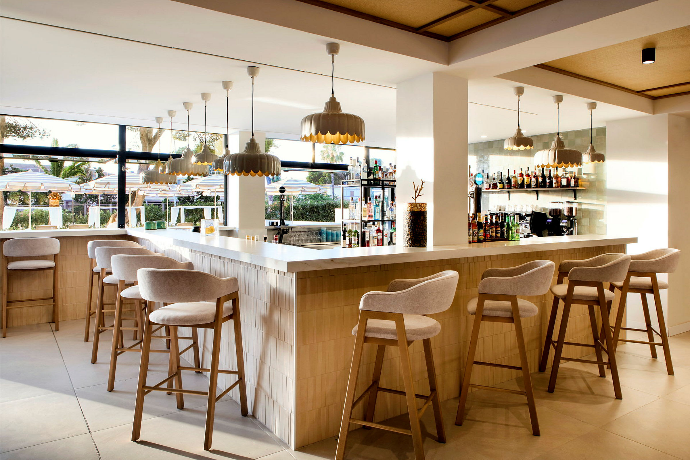 En moderne bar med barstole, hængende lamper og udsigt til en udendørspool. (AI-genereret tekst)