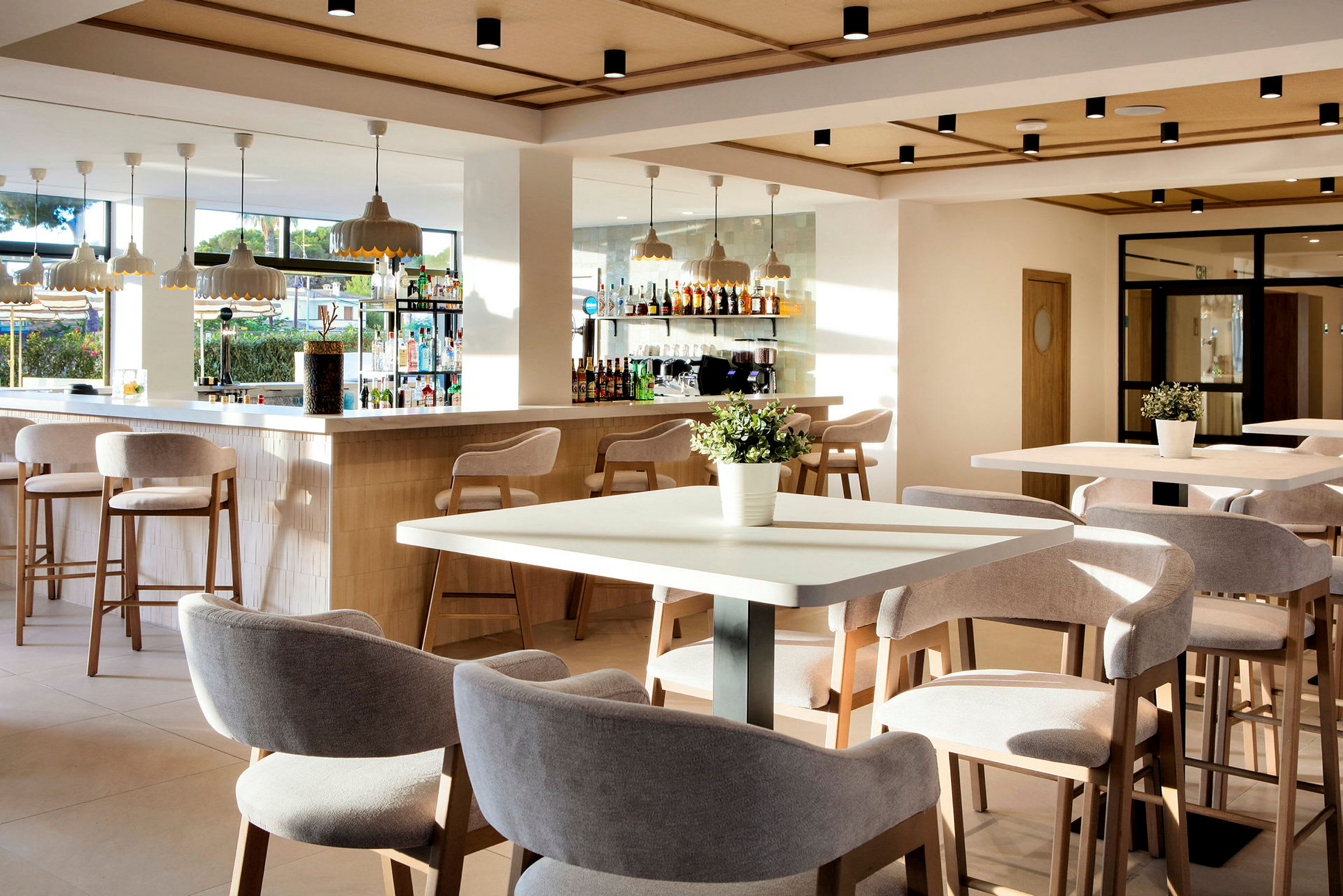 En lys og moderne bar og restaurant med siddepladser ved borde og bar samt dekorative detaljer som blomsterpotter. (AI-genereret tekst)