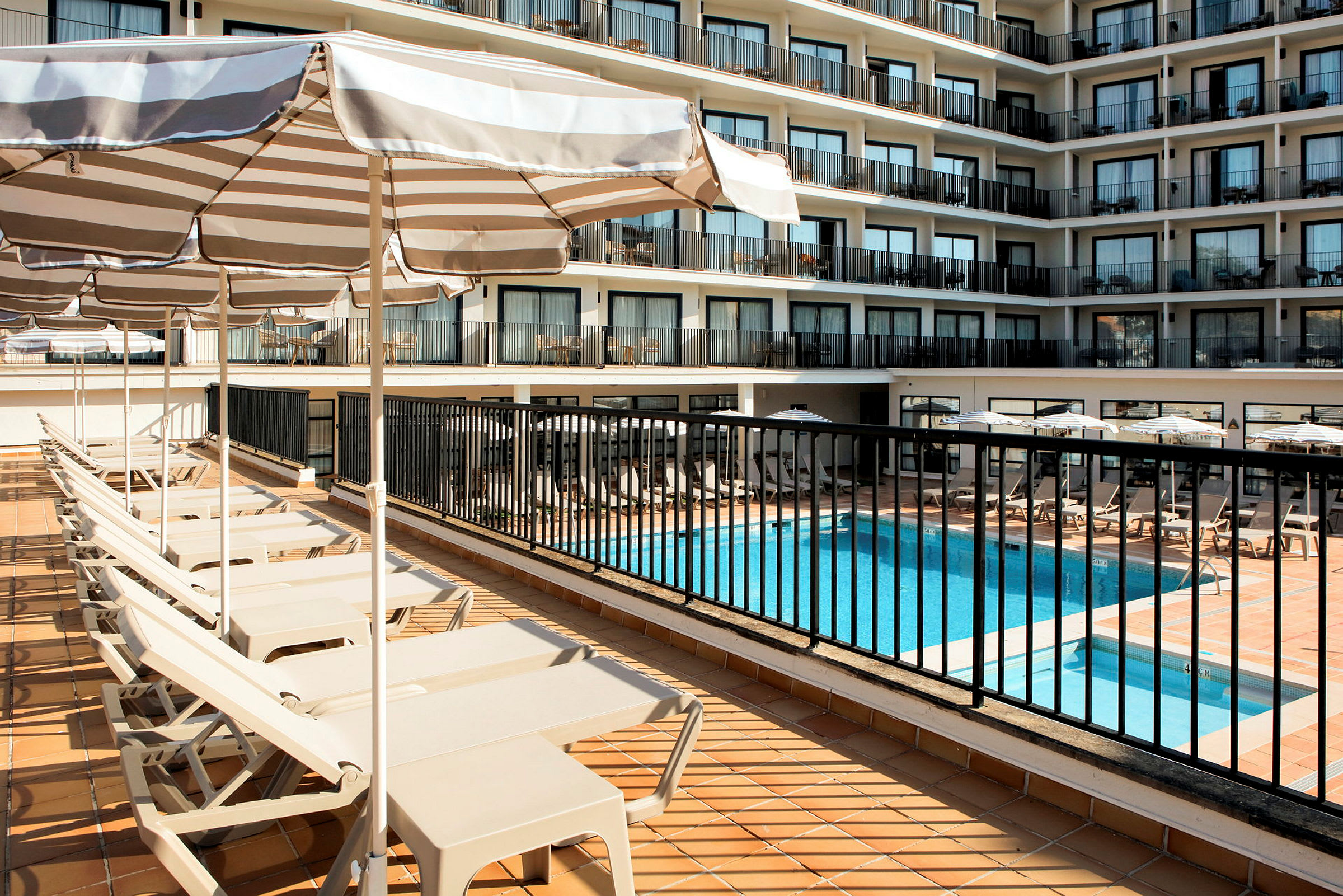 Udsigt over hotelpoolområde og liggestole med parasoller. (AI-genereret tekst)